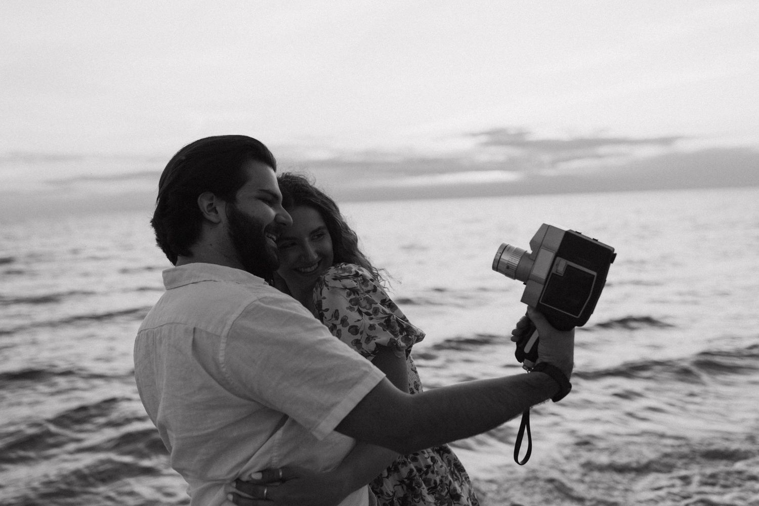 Couple embracing while taking photos on a beach at sunset.