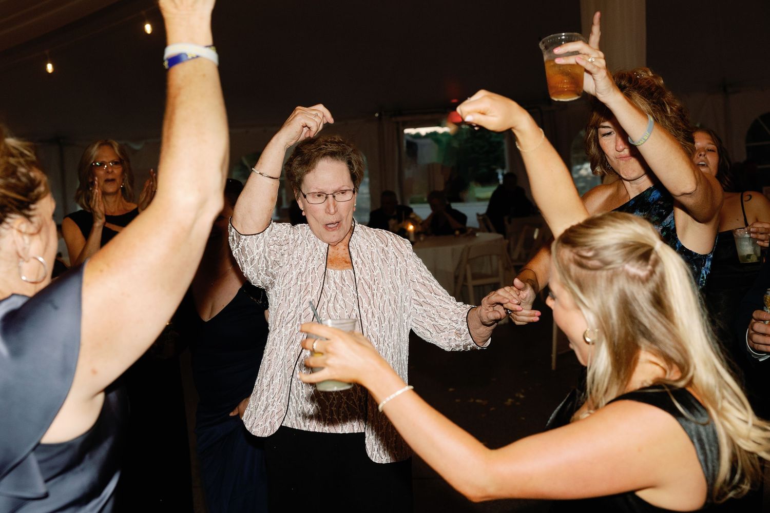 Party guests dancing and celebrating at a dimly lit indoor wedding reception.