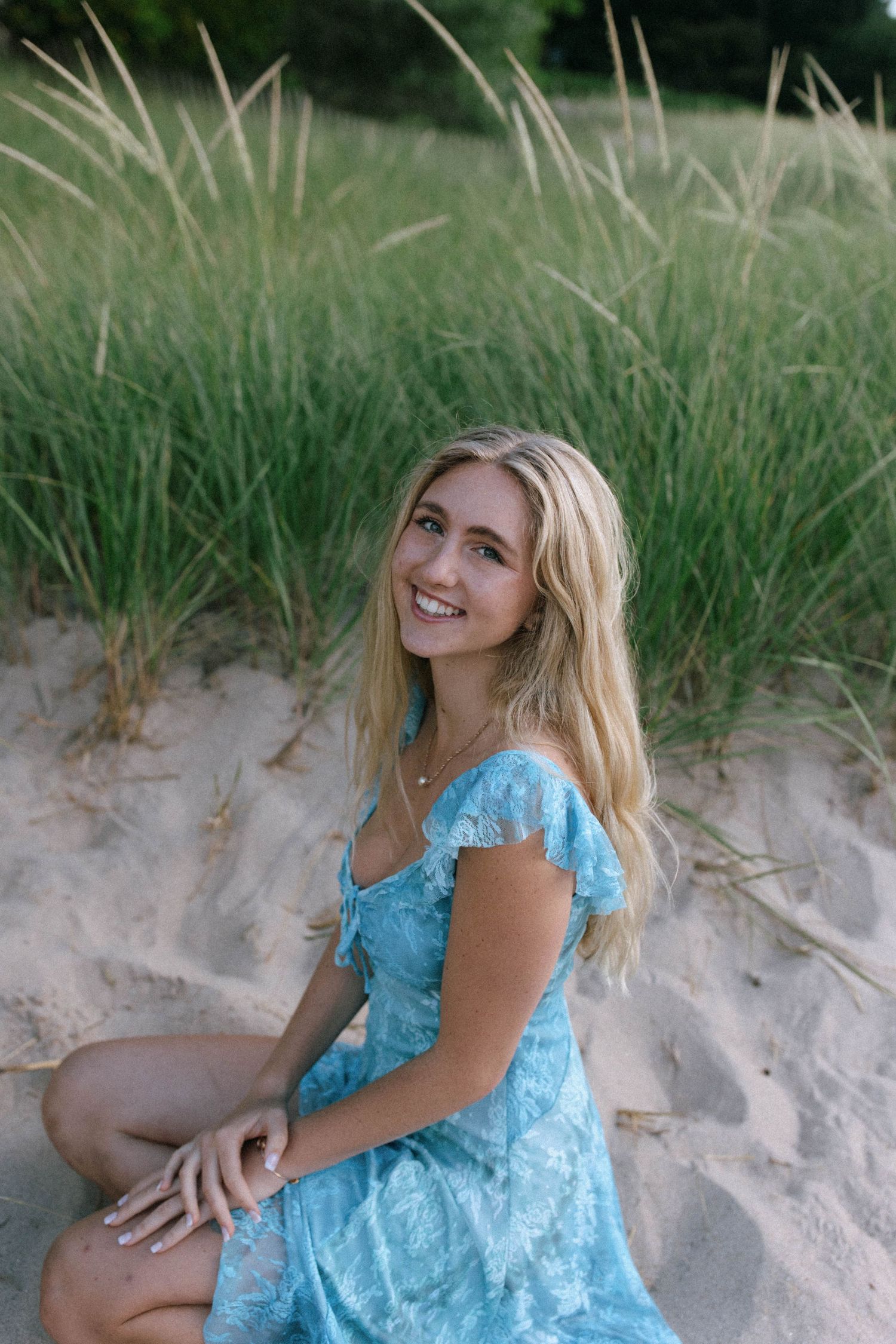 Woman in light blue lace dress poses on sandy beach dunes during golden hour photoshoot.