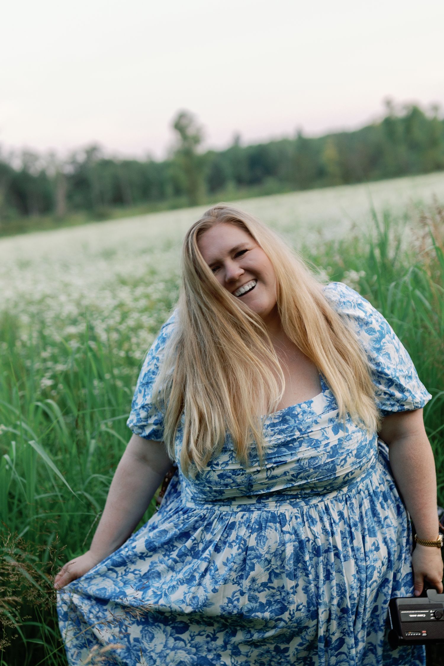A person wearing a blue floral dress poses joyfully in a flowering meadow.