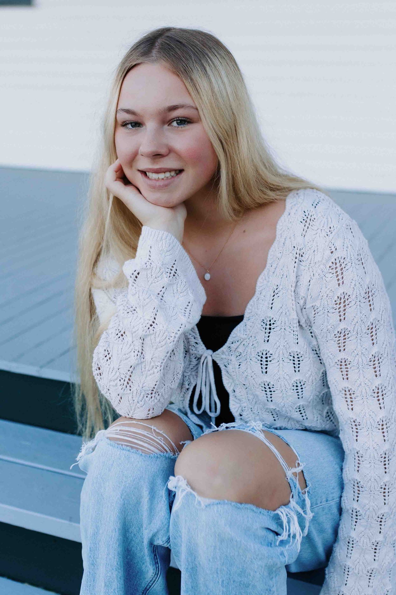 Casual poses on a porch wearing a white crochet cardigan, black top and light denim jeans.