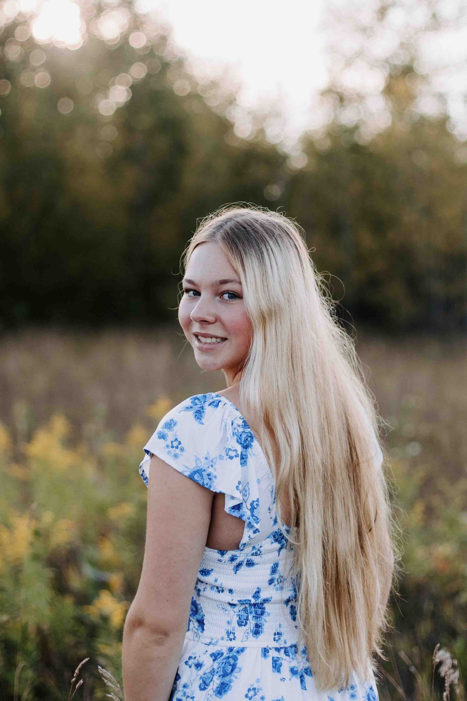 Candid outdoor portrait with blue floral dress in sunlit meadow.