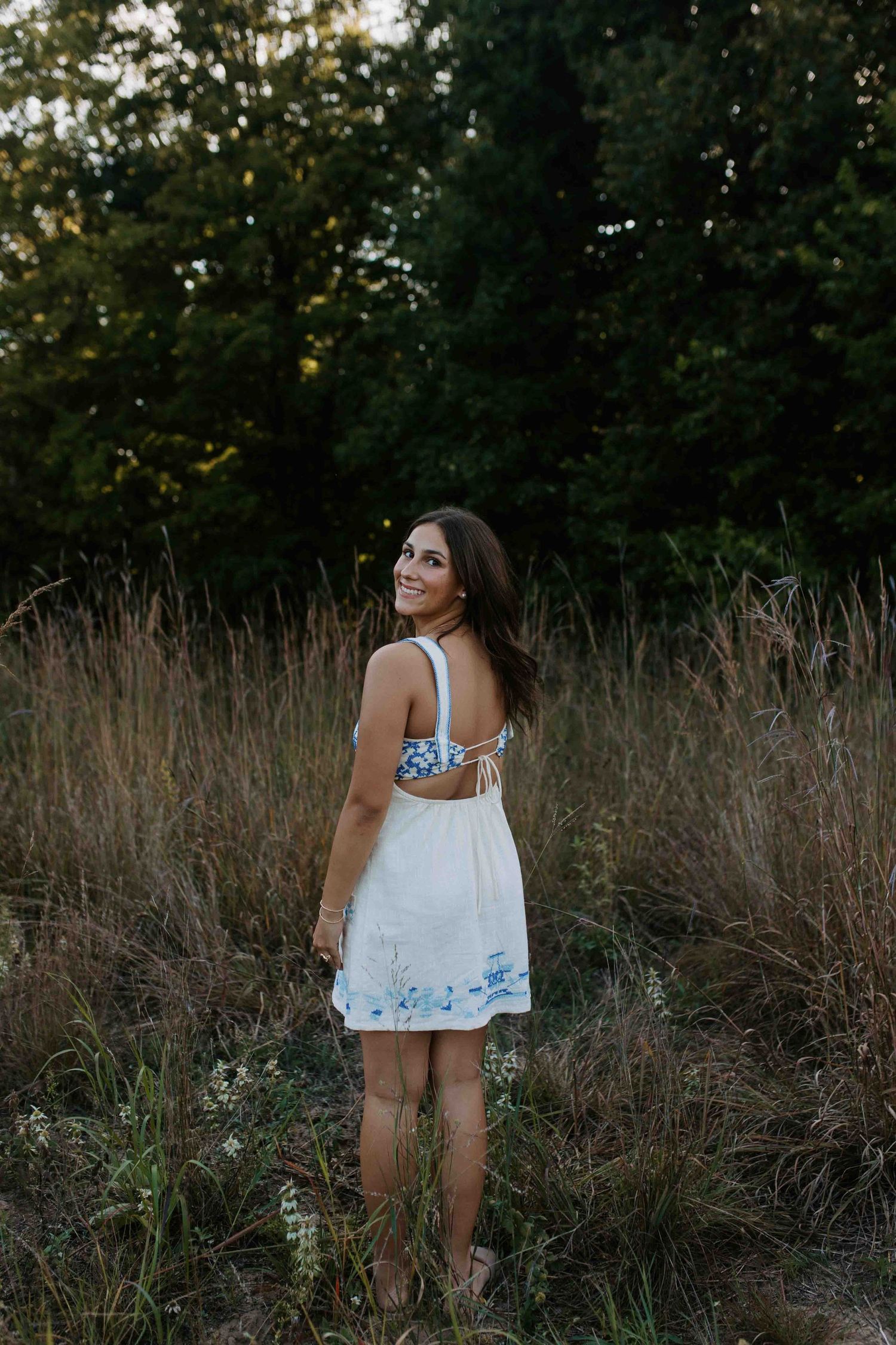 Natural light photography of a summery white dress with blue accents in a meadow setting.