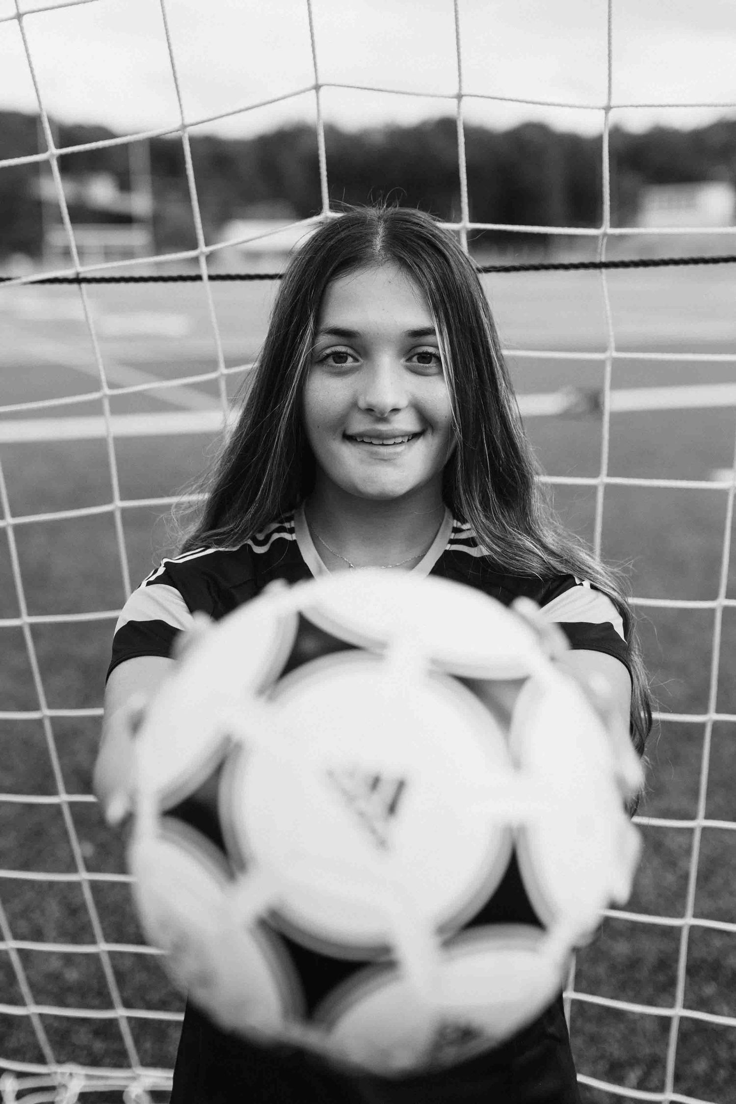 Black and white photo of soccer player holding multiple balls in front of goal net.