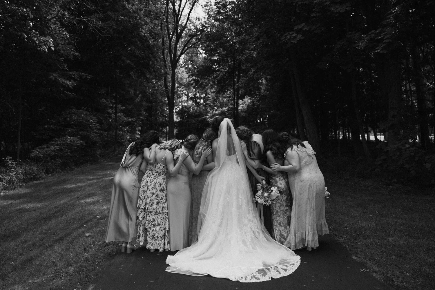 Wedding party poses for dramatic black and white panoramic photos in an outdoor garden setting.