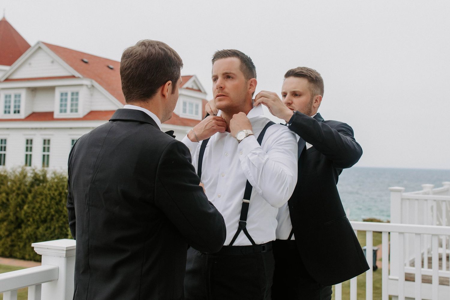 Formal wedding party gathered on a coastal property with white houses in background.