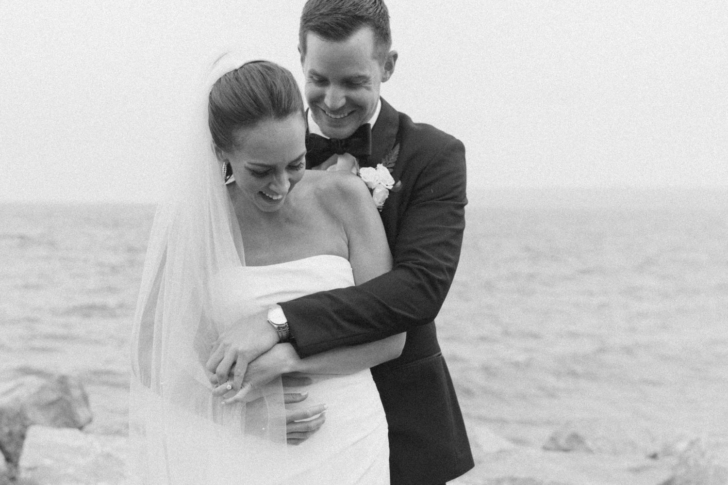 Black and white wedding photo capturing an intimate embrace by the sea.