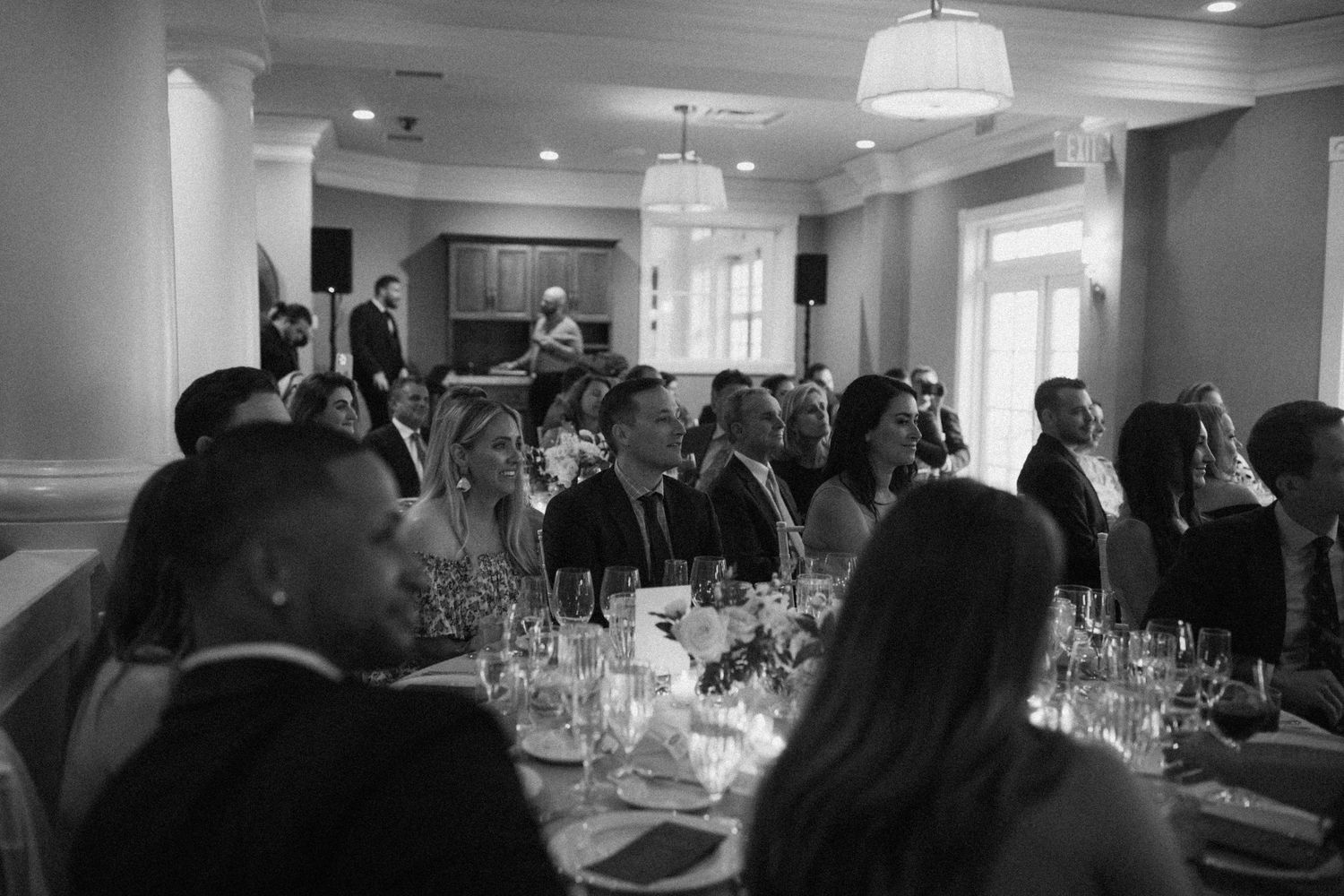 Wedding reception guests seated at elegantly decorated tables in a bright banquet room.