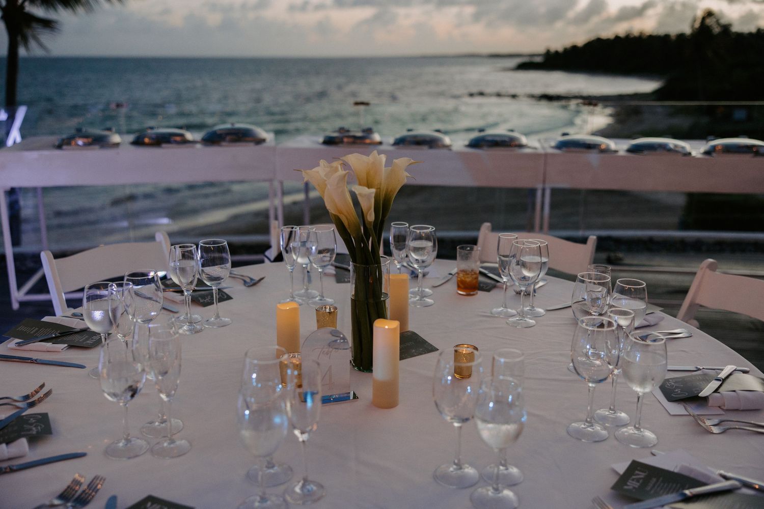Elegant wedding reception table settings with glassware and centerpieces overlooking the ocean.