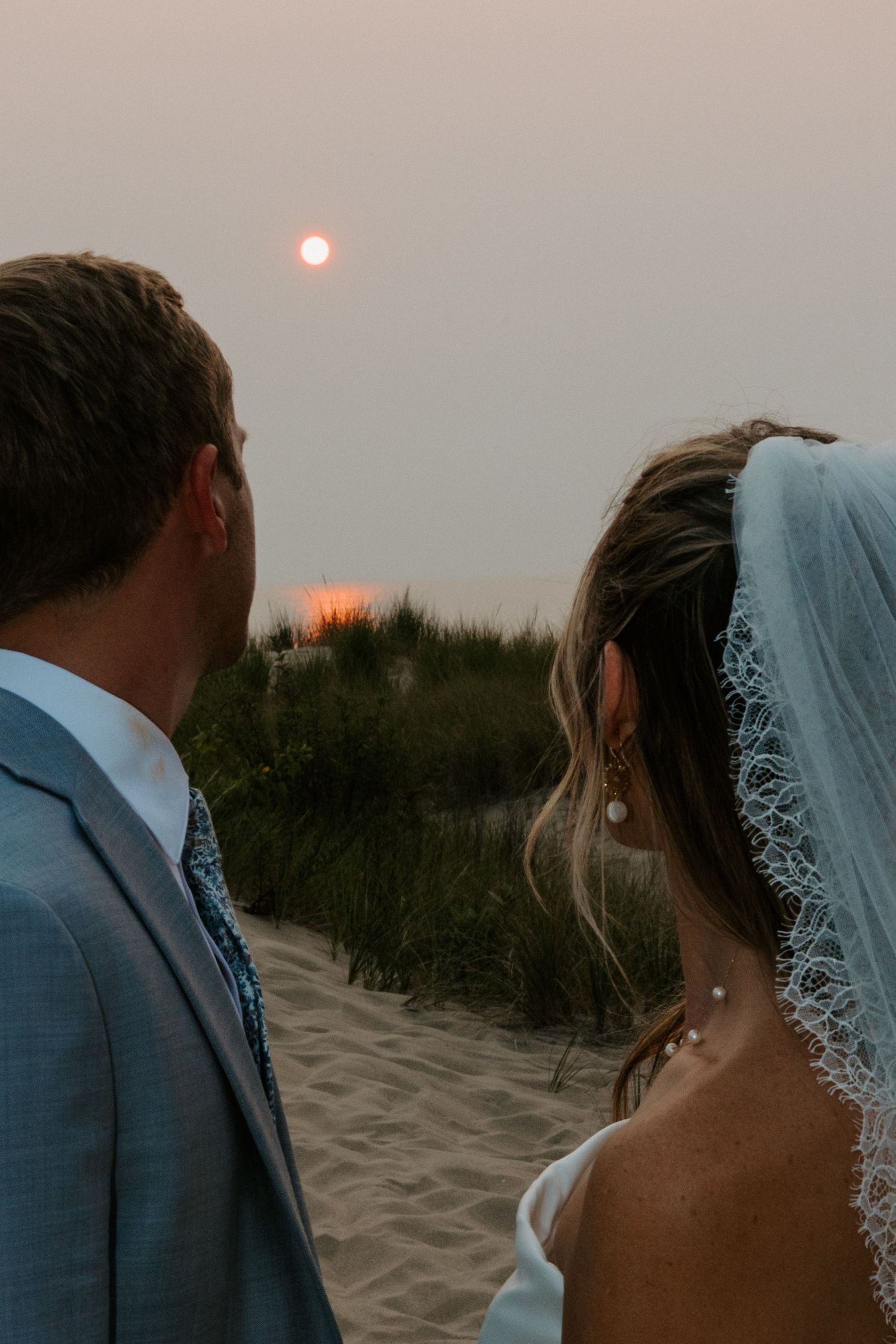 Intimate sunset beach wedding portraits with soft lighting and delicate lace veil details.