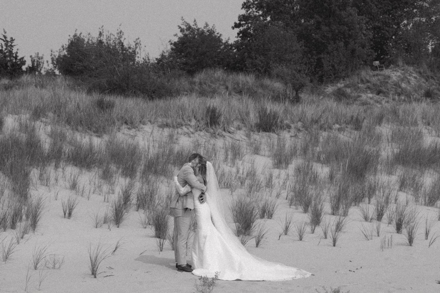 Wedding dress train trails across sandy dunes with beach grass in the background.