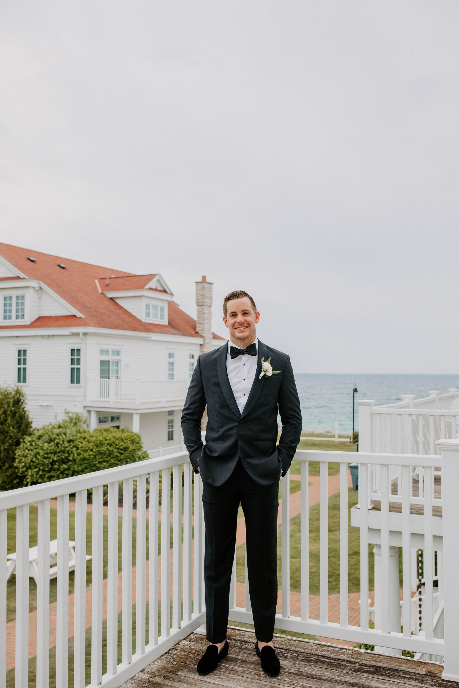 Wedding party members in formal attire standing on a white deck railing overlooking the ocean.