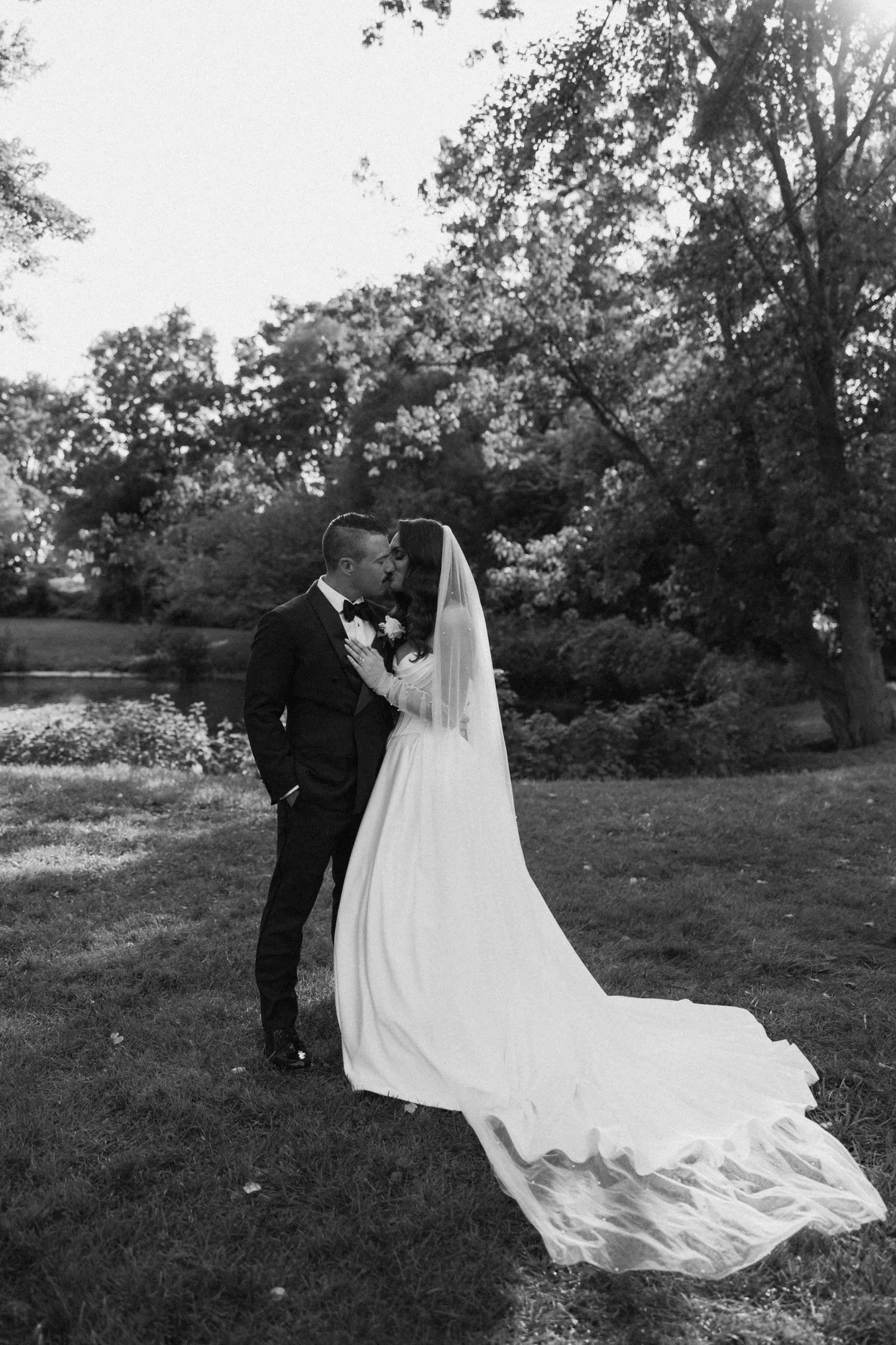 Black and white photo of wedding dress train flowing across grassy field.