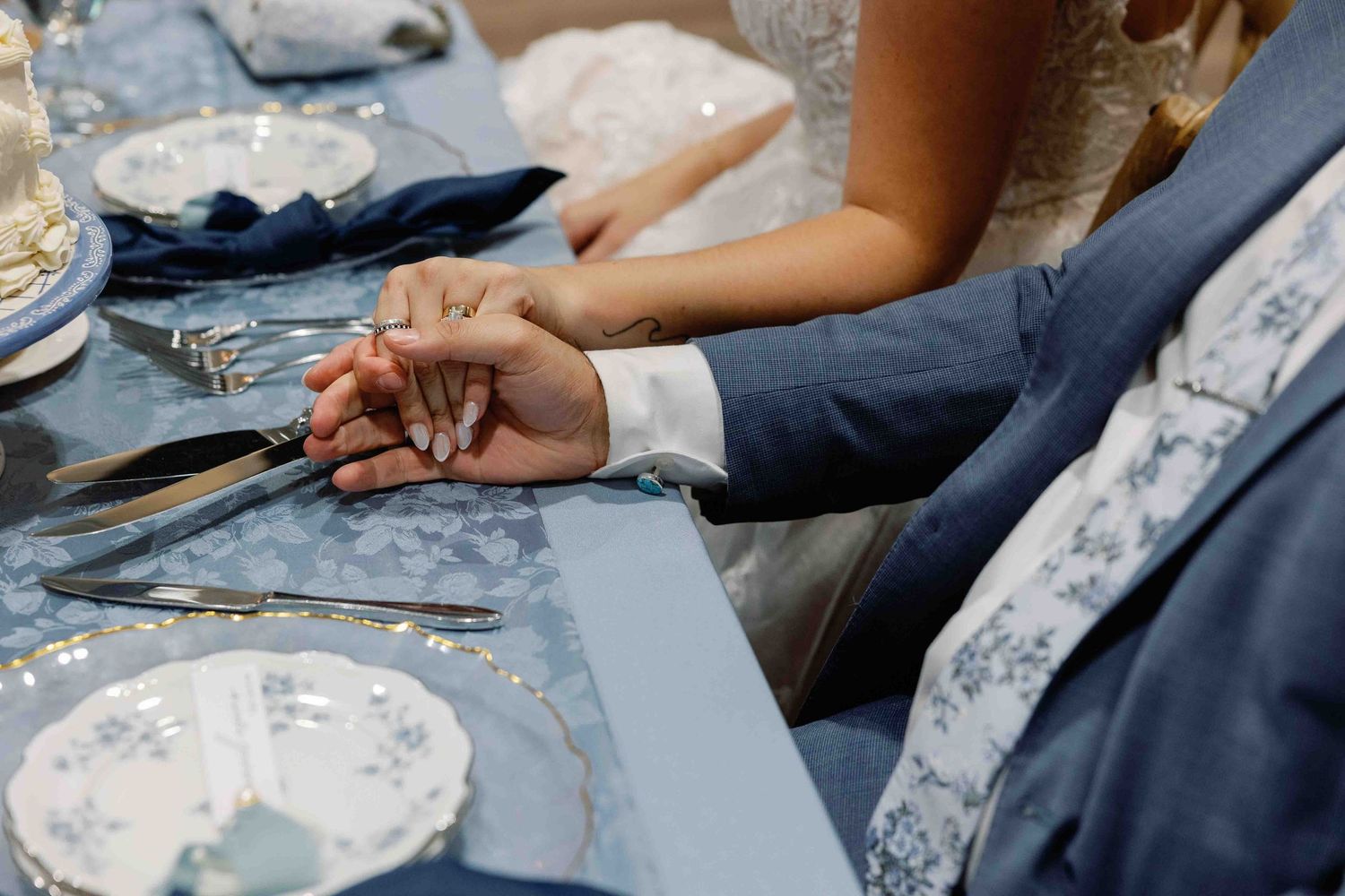 Close-up of hands resting on a blue and white patterned tablecloth at a wedding reception.
