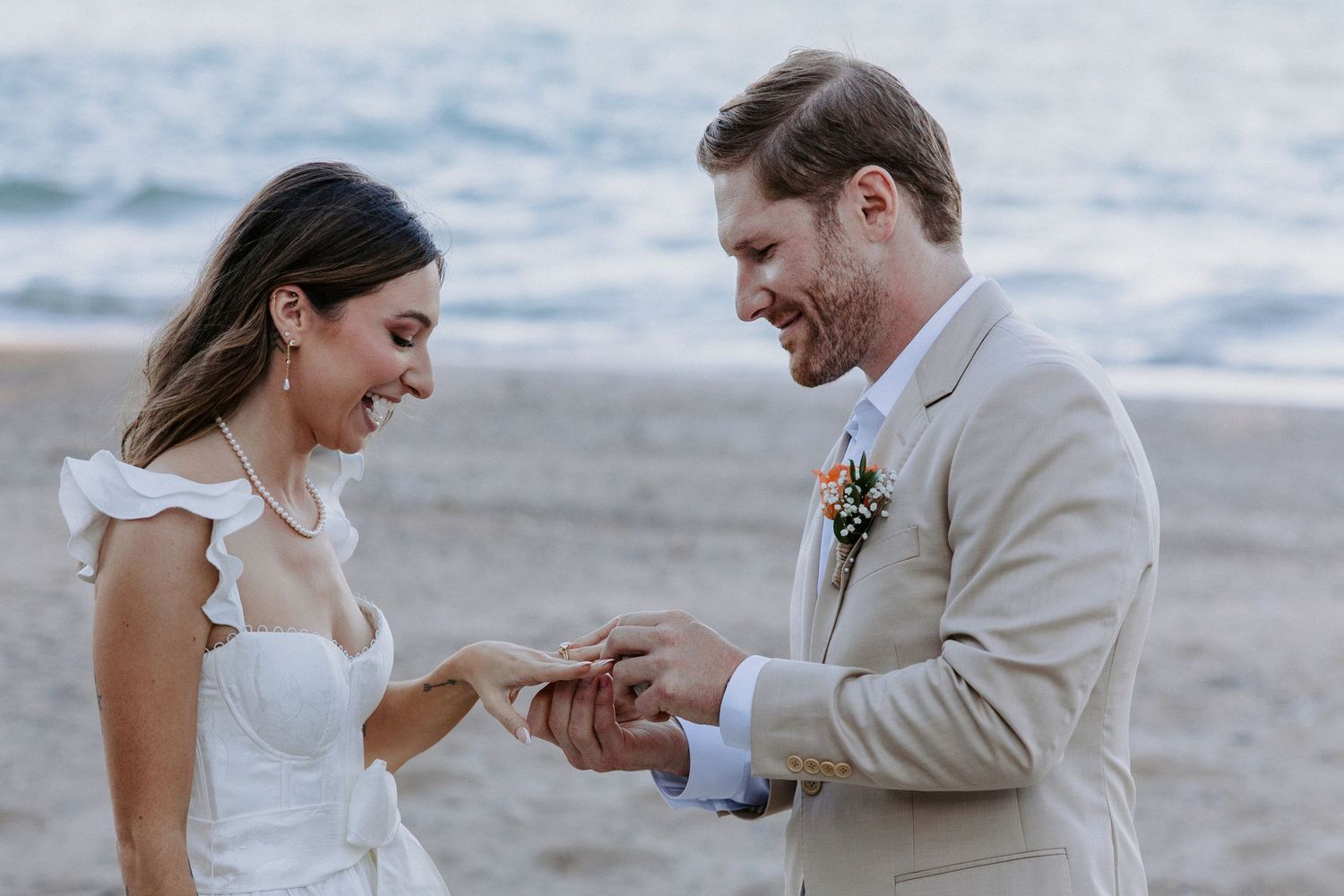 Romantic beach wedding photo session with couple in white dress and beige suit by the ocean.