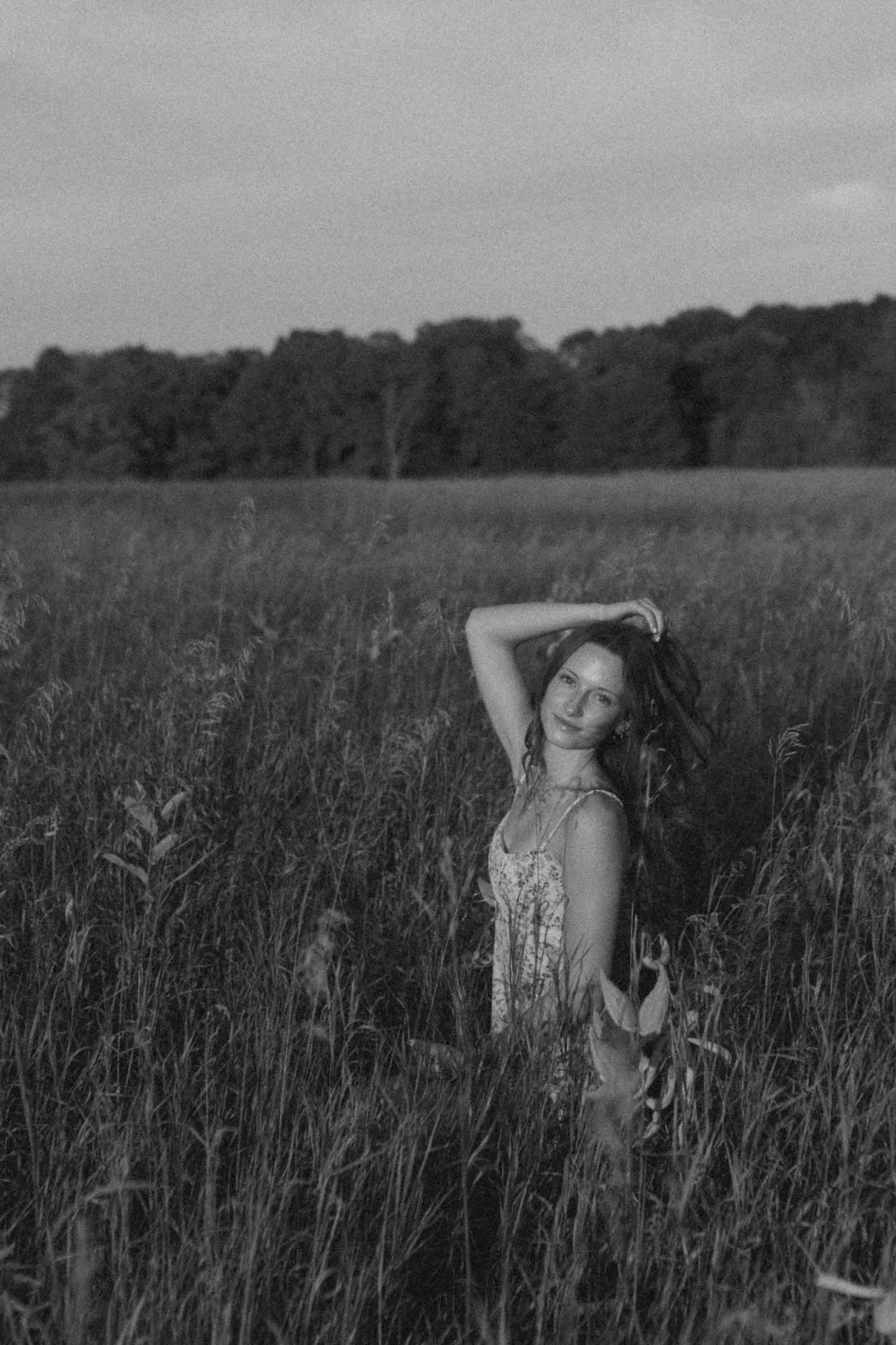 Black and white portrait of someone posing in a field of tall grass at sunset.