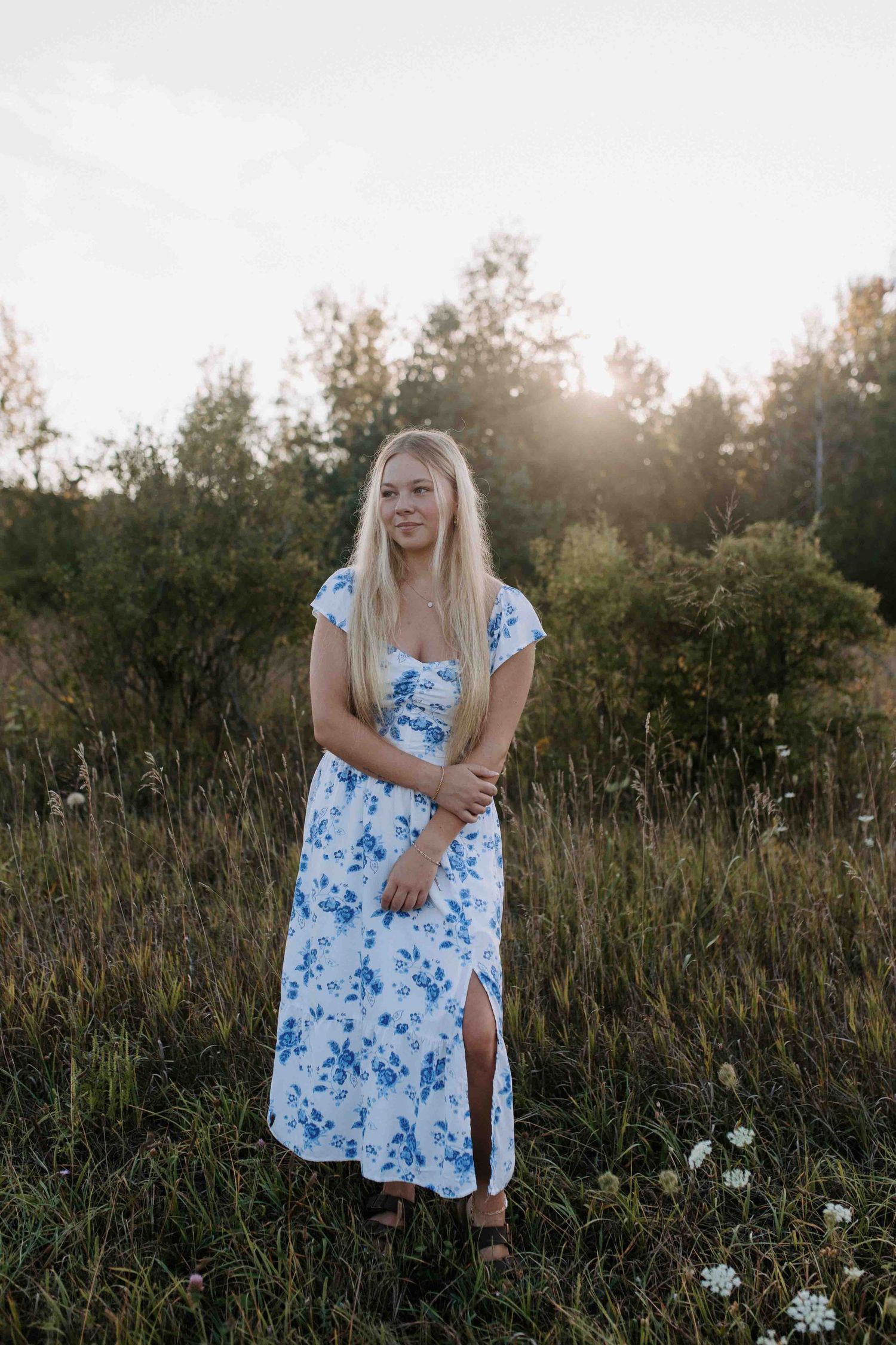 A summer photoshoot in a field at golden hour featuring a blue and white floral maxi dress.