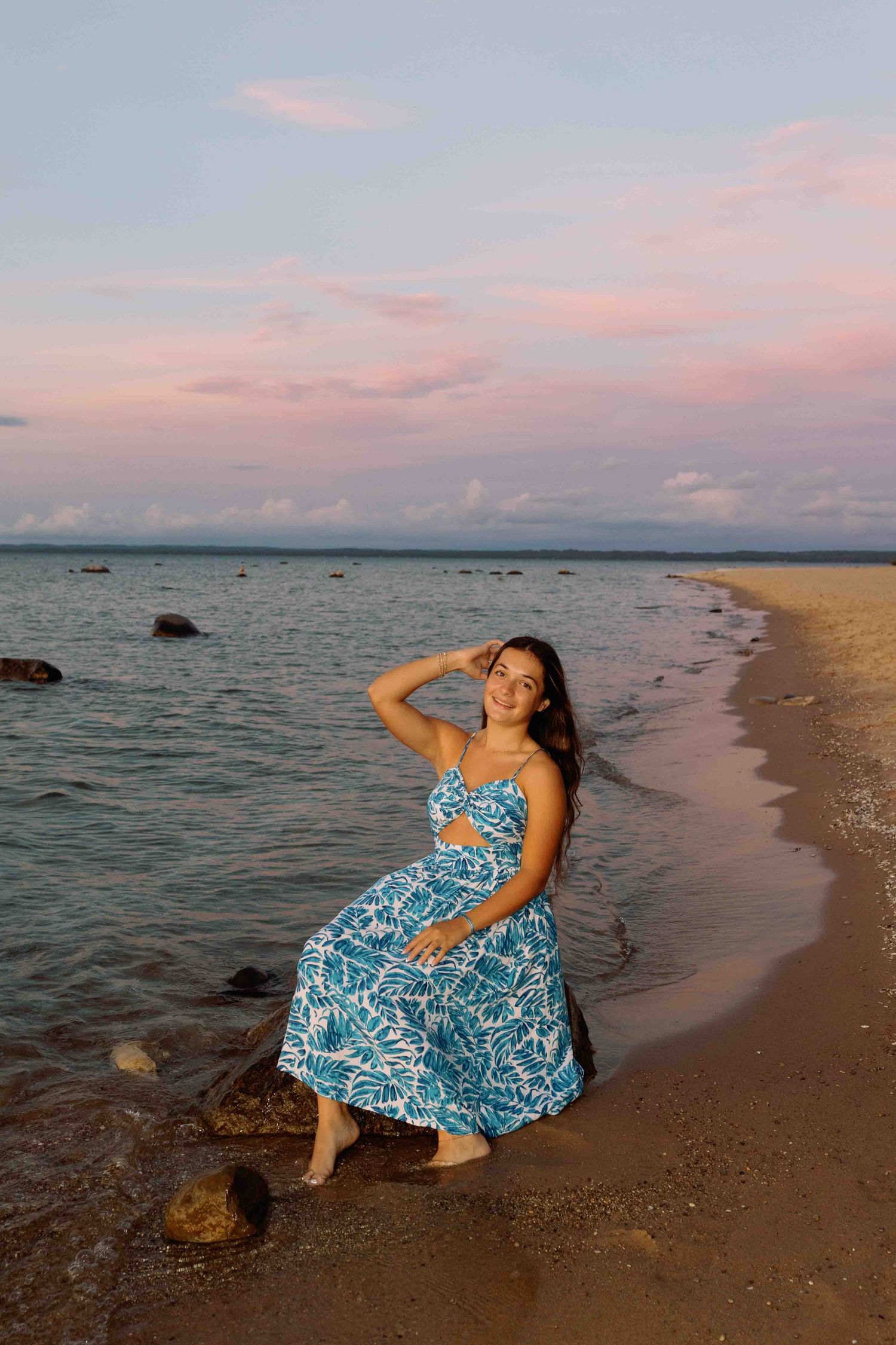 Beachside portrait session at dusk with pink clouds and rocky shoreline.