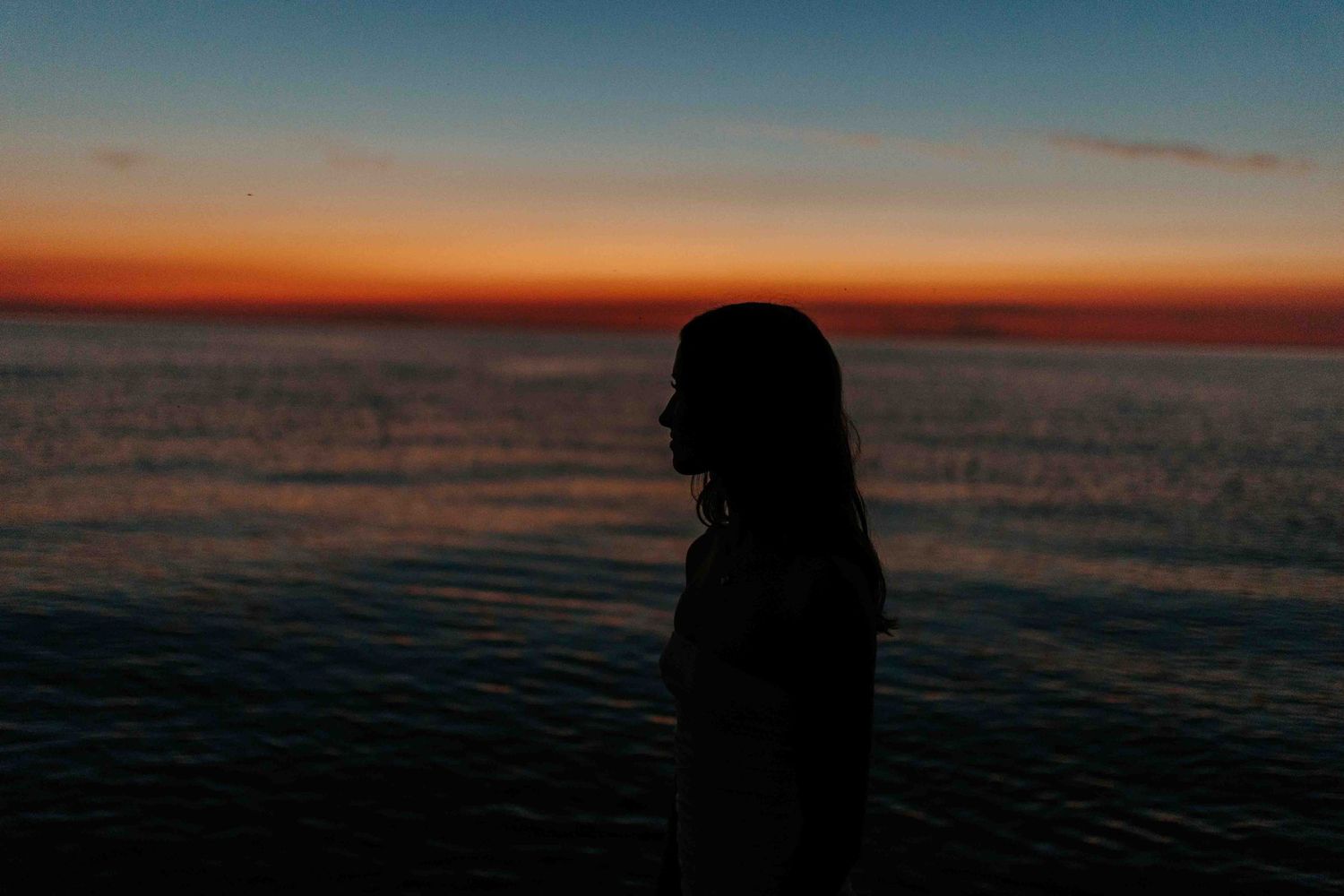 Silhouettes against a dramatic sunset sky over the ocean create a moody beach scene.