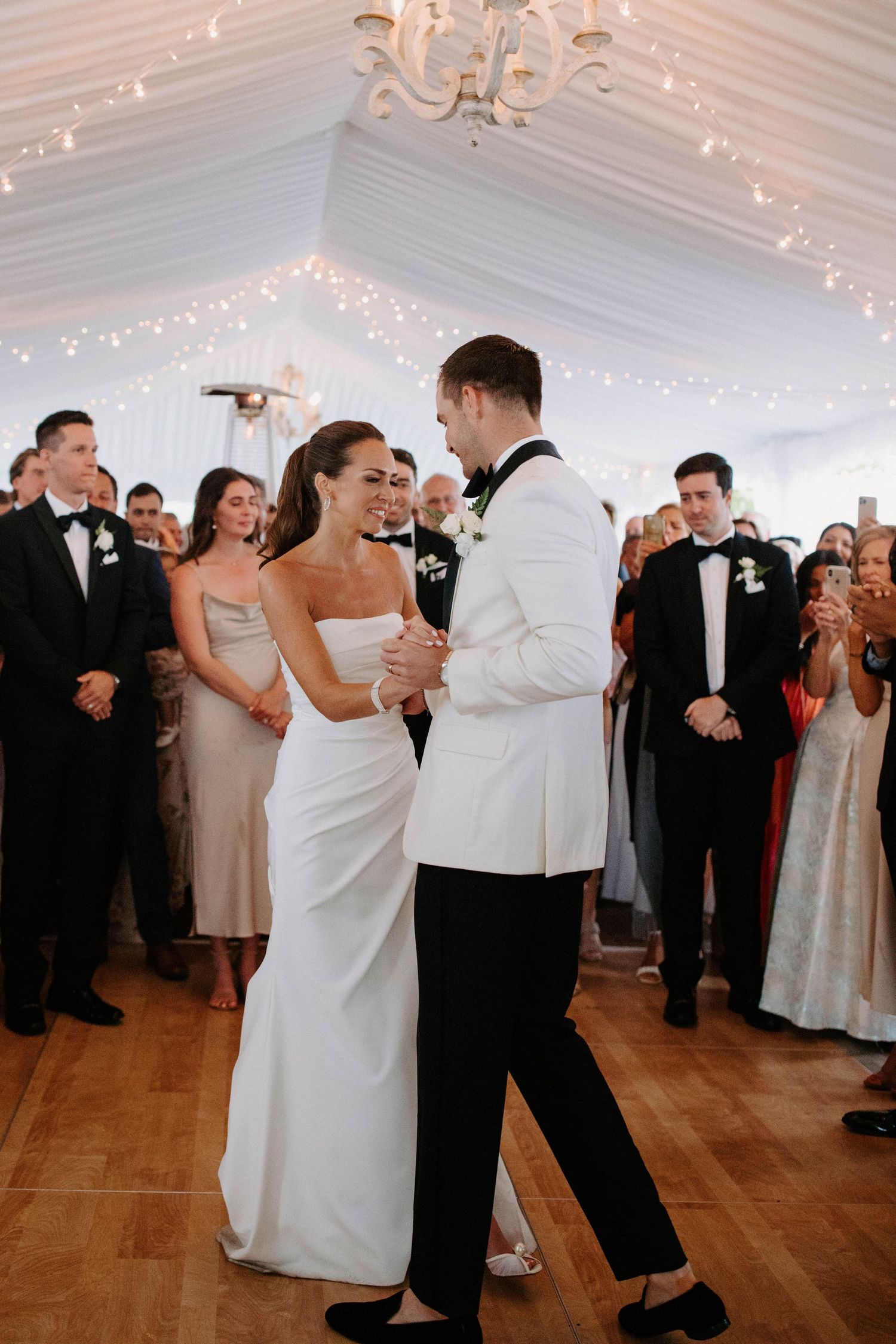 Wedding guests enjoying a lively dance party in a white tent venue with string lights overhead.
