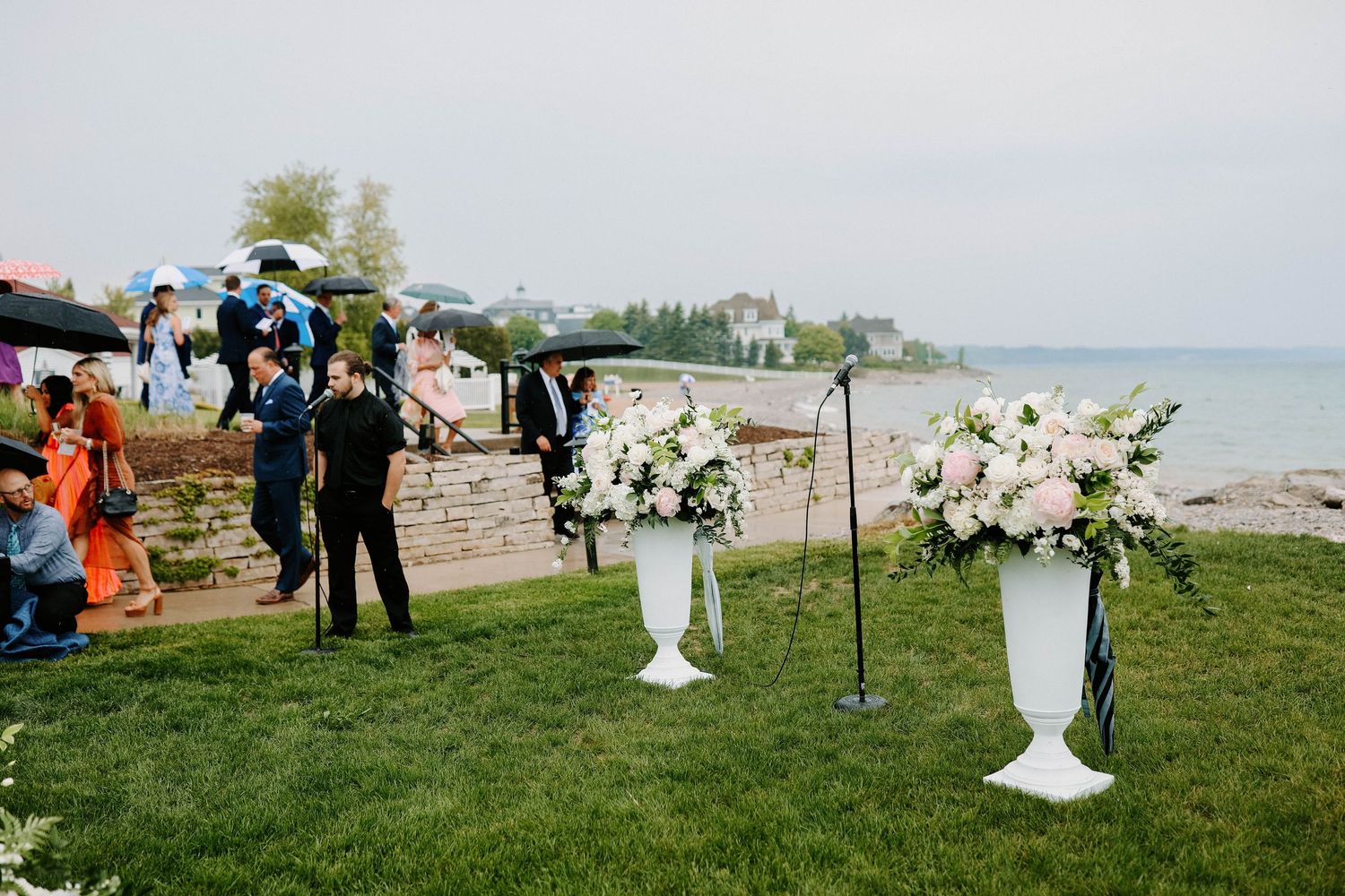 Outdoor wedding ceremony setup with white pedestals and floral arrangements by the ocean.