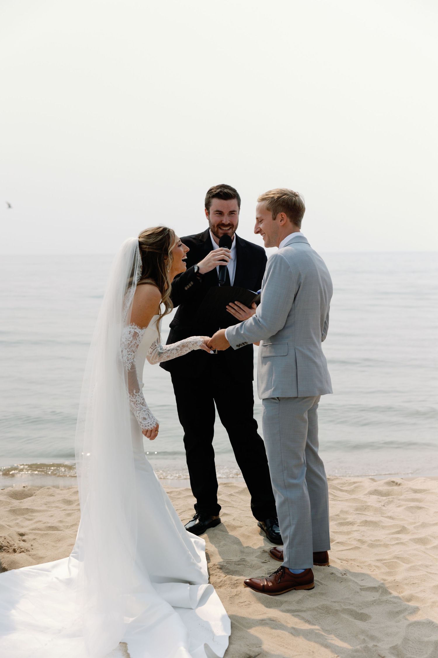 Beach wedding ceremony with officiant and couple exchanging vows by the ocean.