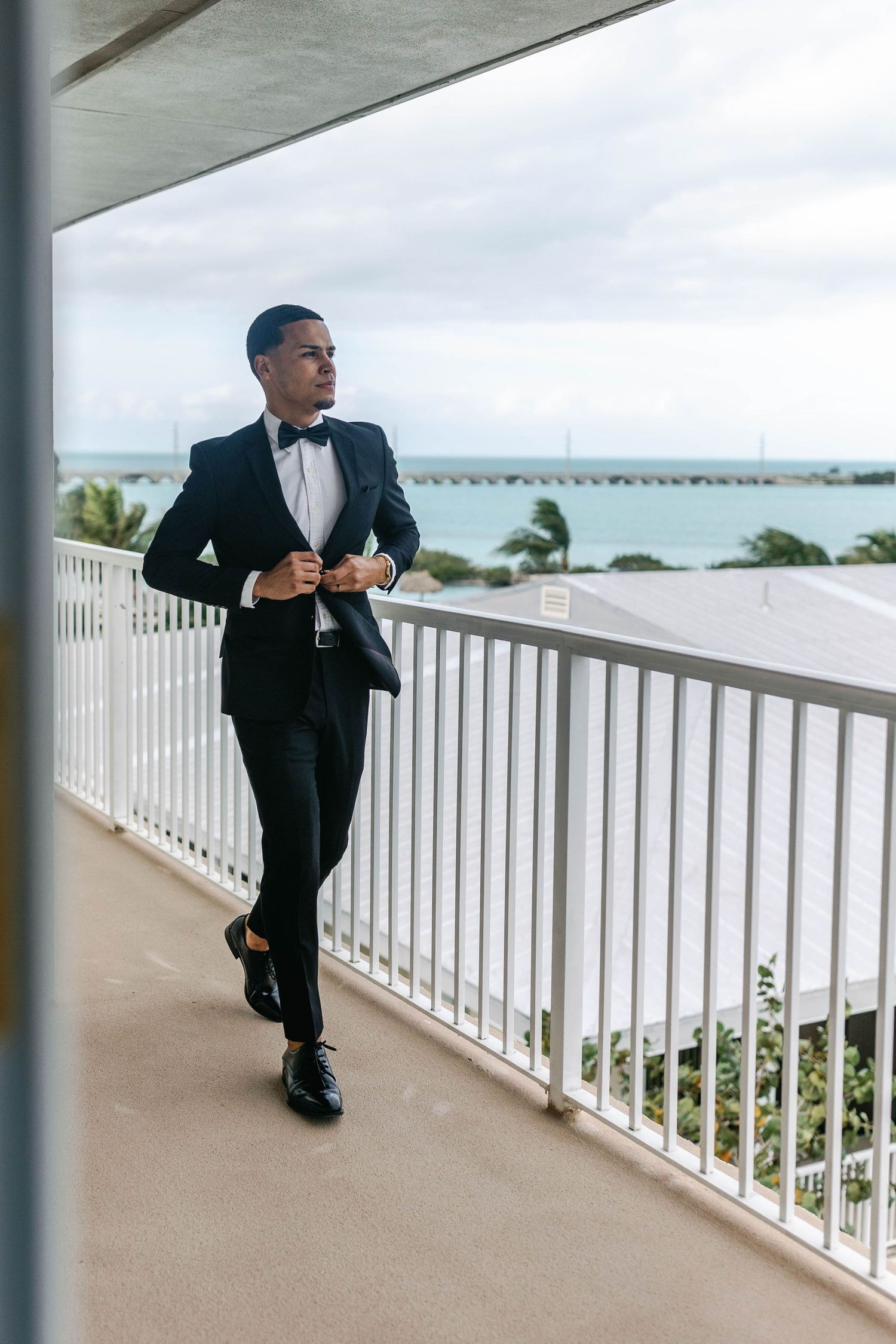 A formal event space with a white railing balcony overlooking the ocean and palm trees on a cloudy day.