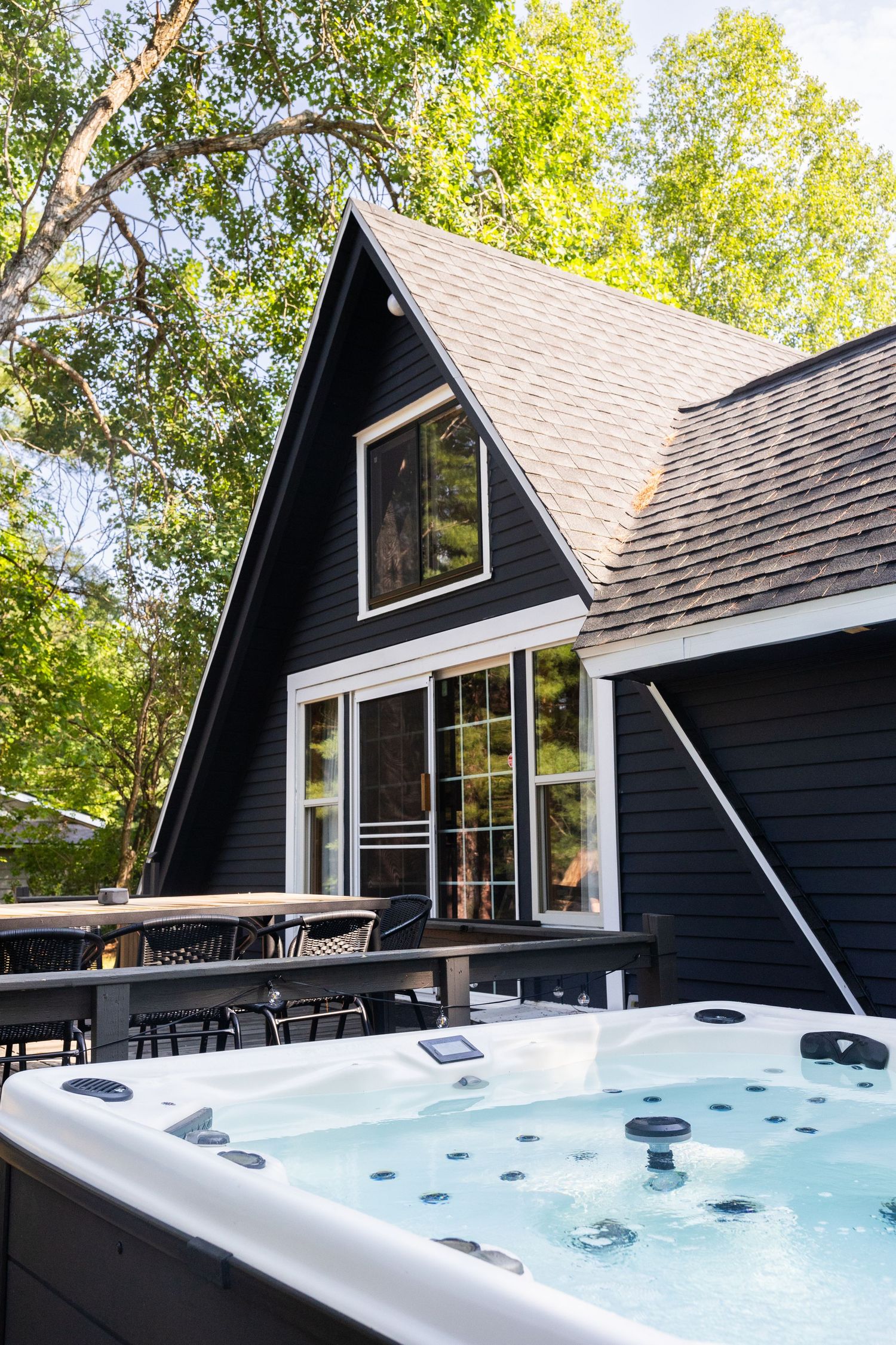Modern A-frame cabin with black exterior siding and hot tub showcases multiple angles of its stylish outdoor amenities.