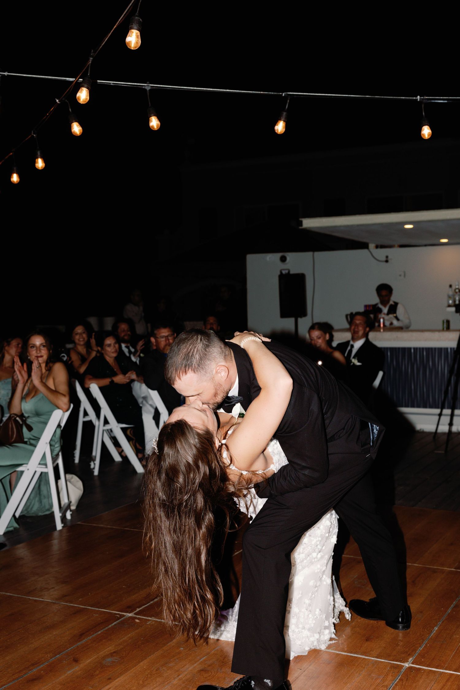 Romantic dip dance move performed during wedding reception under string lights.