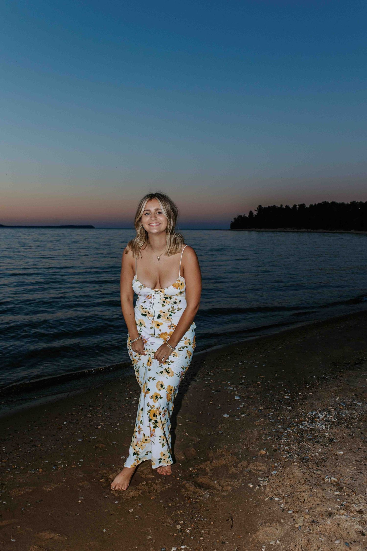 A floral sundress on a beach at sunset with calm waters and distant shoreline in view.