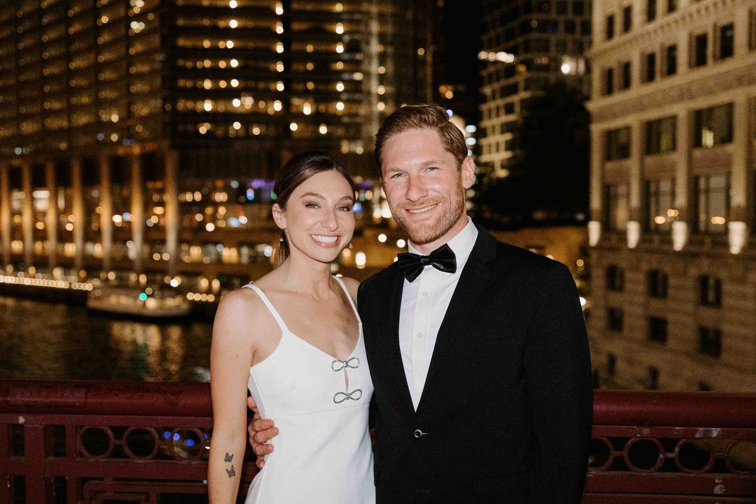 A nighttime cityscape with a couple posing in formal attire against illuminated buildings.