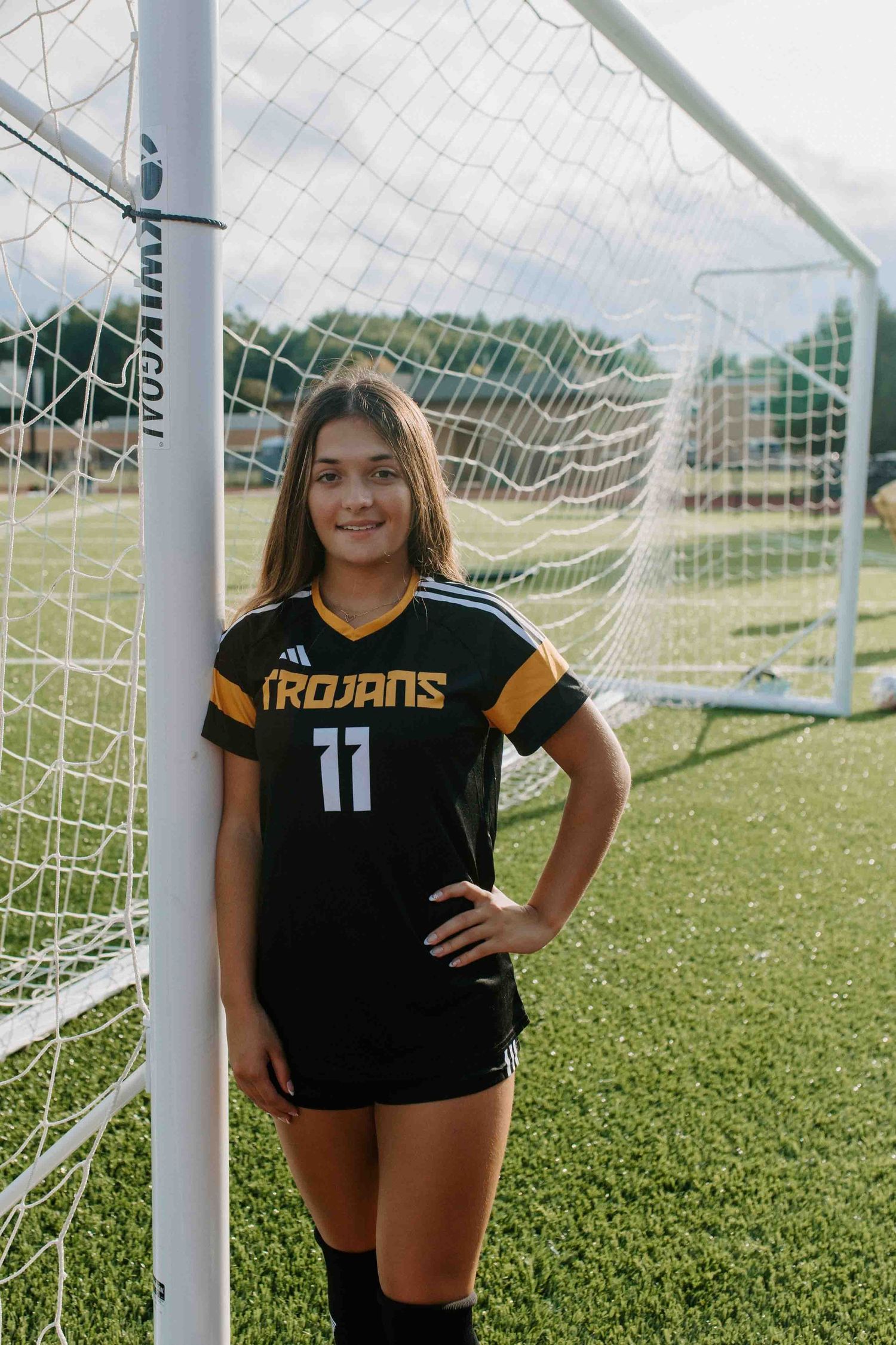Soccer player poses by goal net in black Trojans uniform number 11.