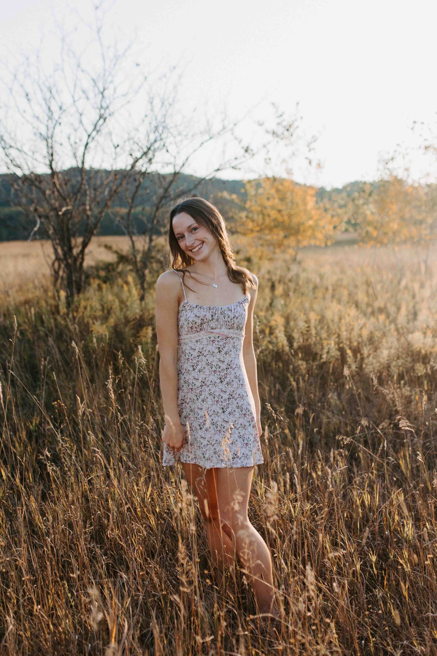 Someone wearing a floral summer dress poses in a rustic field at dusk.
