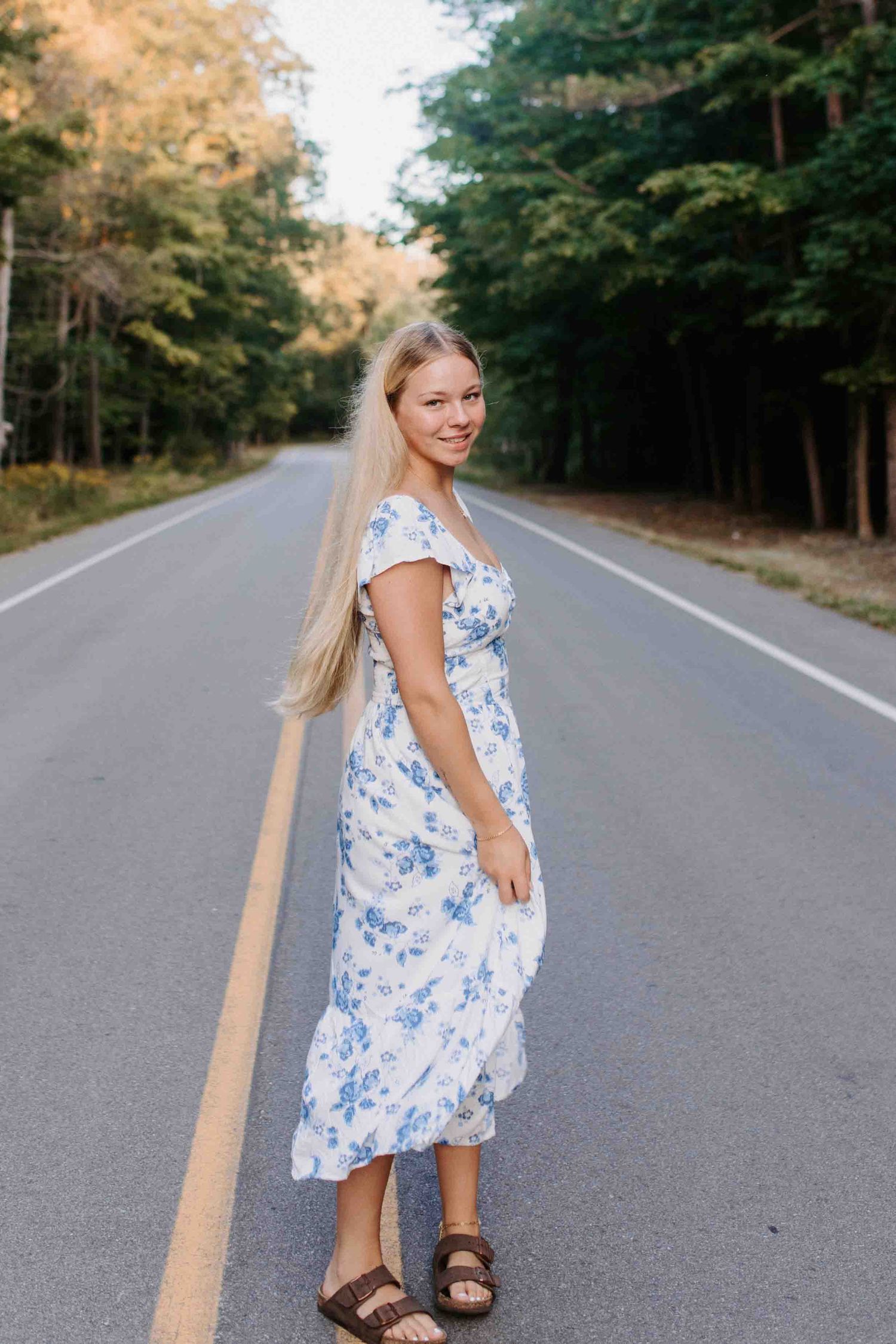 Person in a summer dress stands on an empty forest road with sandals.