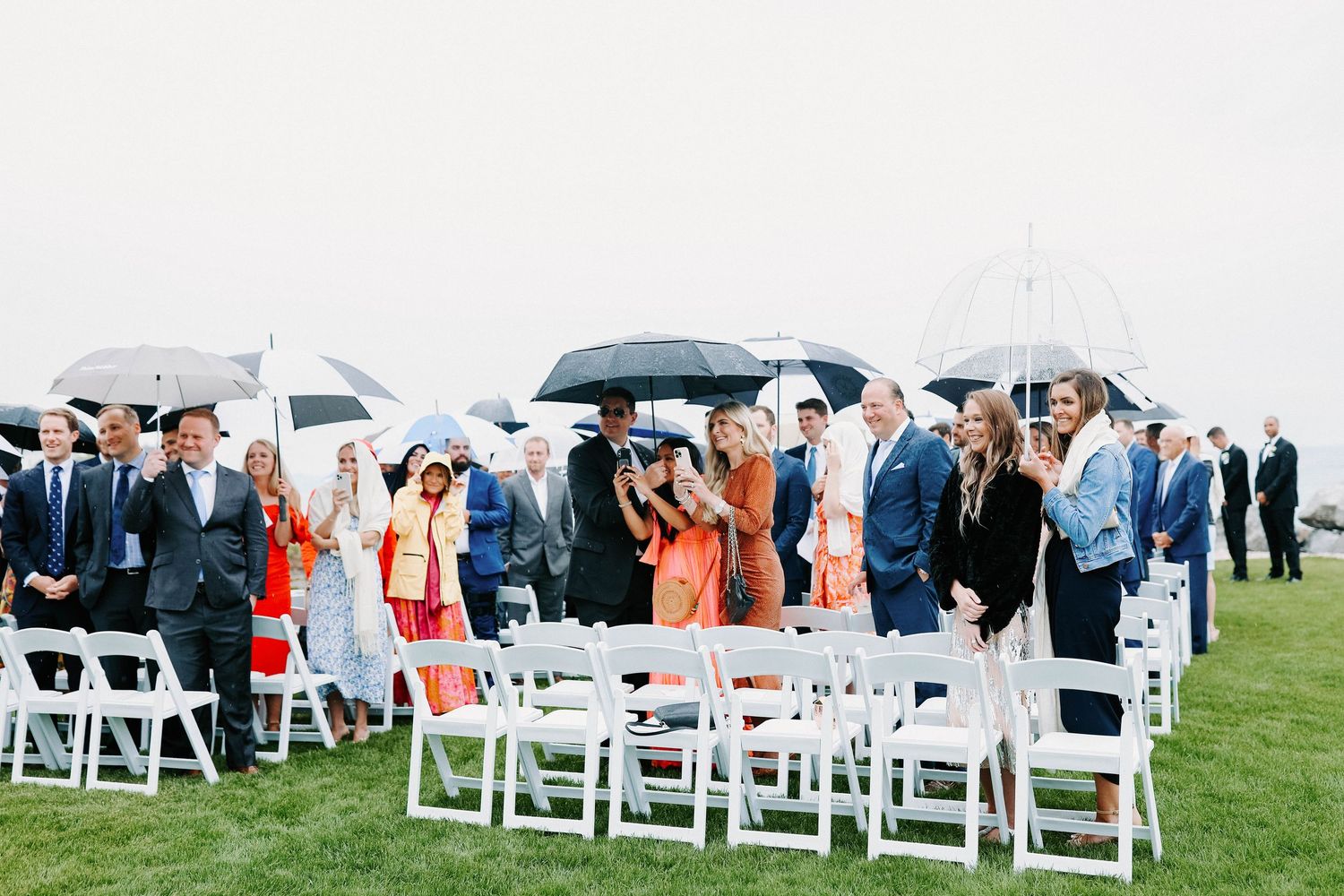 Wide view of wedding guests seated with umbrellas during an outdoor ceremony.