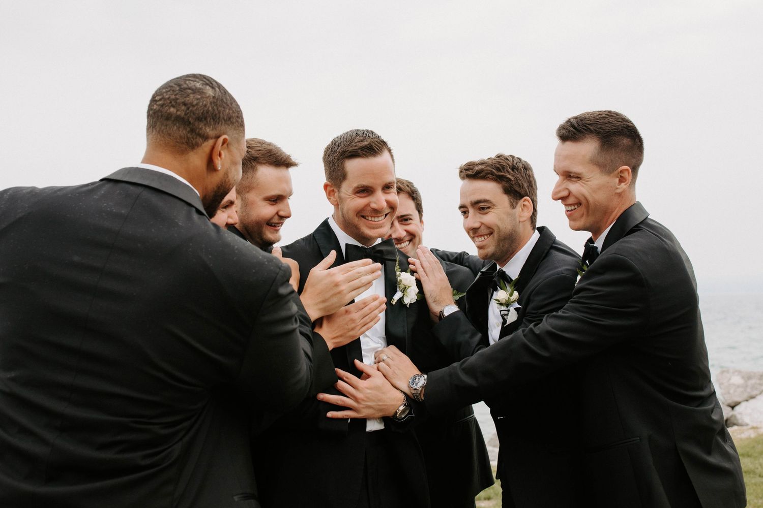 Groomsmen in black suits sharing laughs during wedding celebrations.