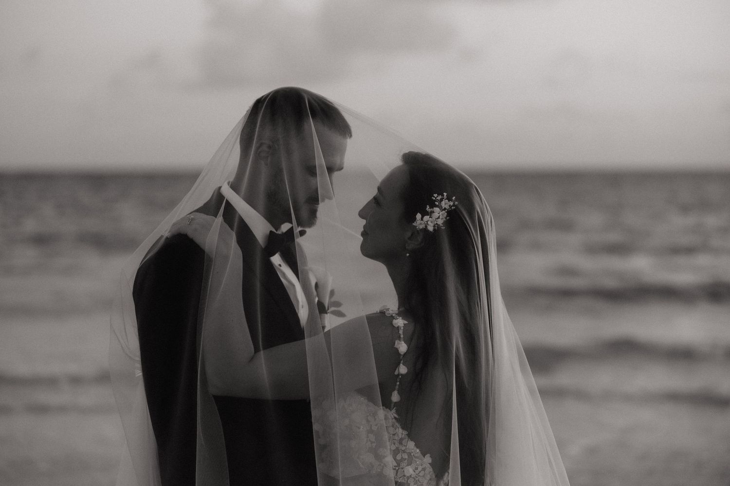 A tender moment between newlyweds on a beach with waves in the background.
