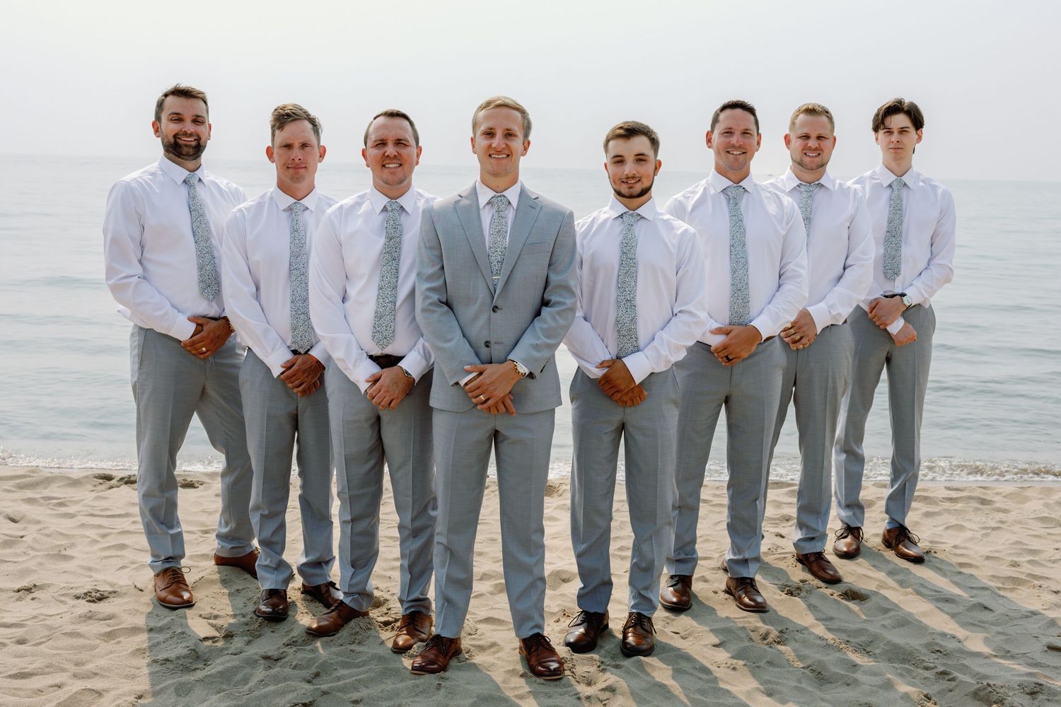 Groomsmen in light gray suits showing off their colorful socks while standing on a beach.