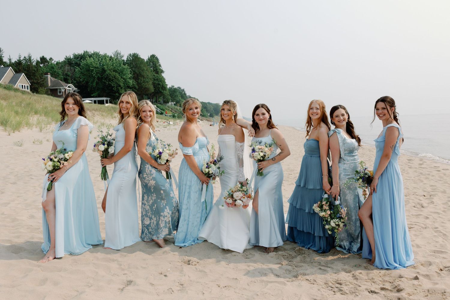Bridesmaids in light blue dresses posing together on beach sand.