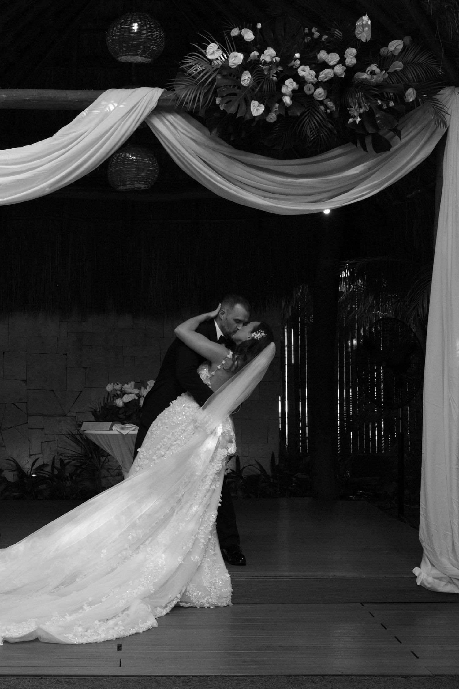 Dramatic dip pose during wedding first dance under elegant white draping and floral decor.