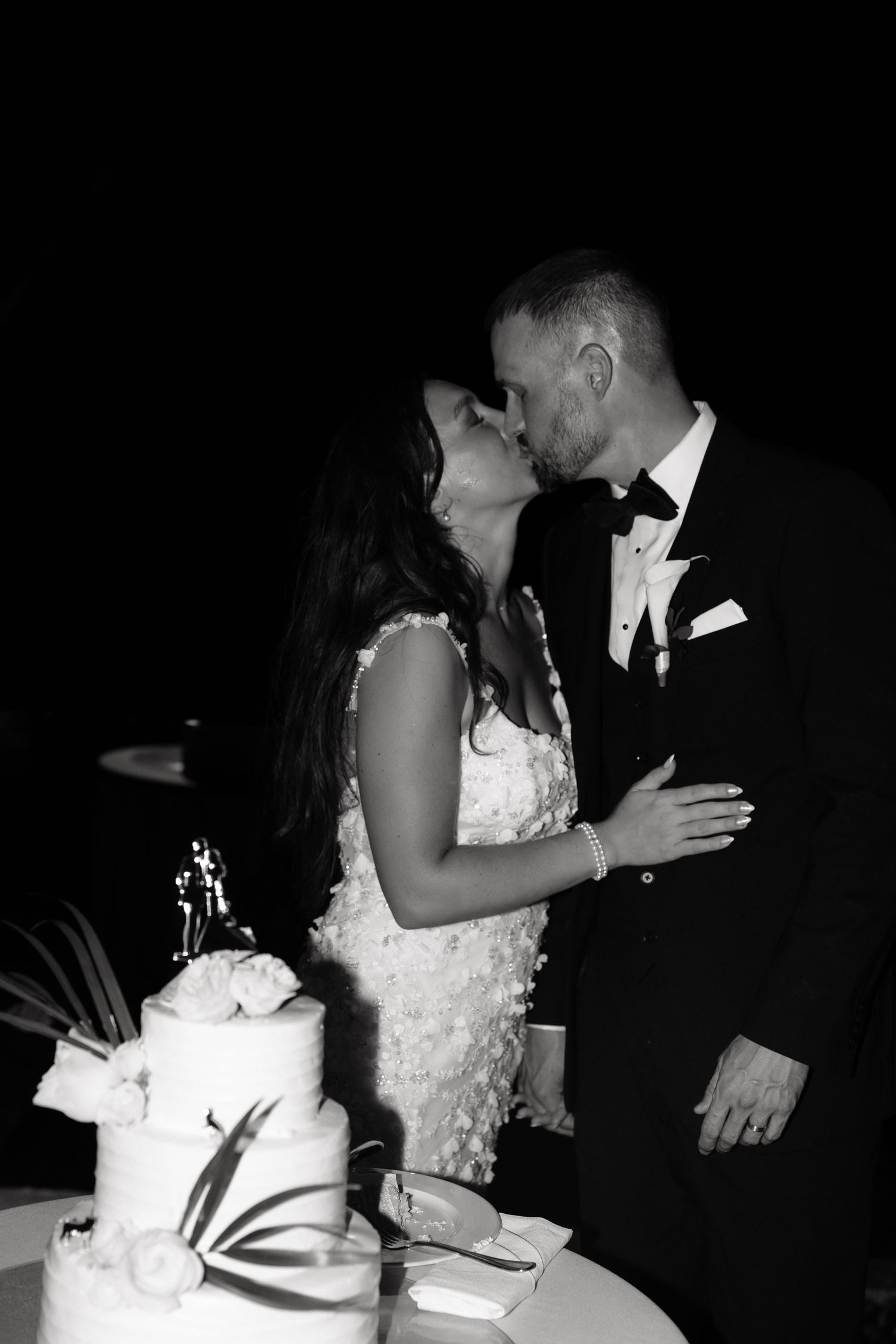 A romantic moment between newlyweds sharing their first kiss next to their elegant white wedding cake.