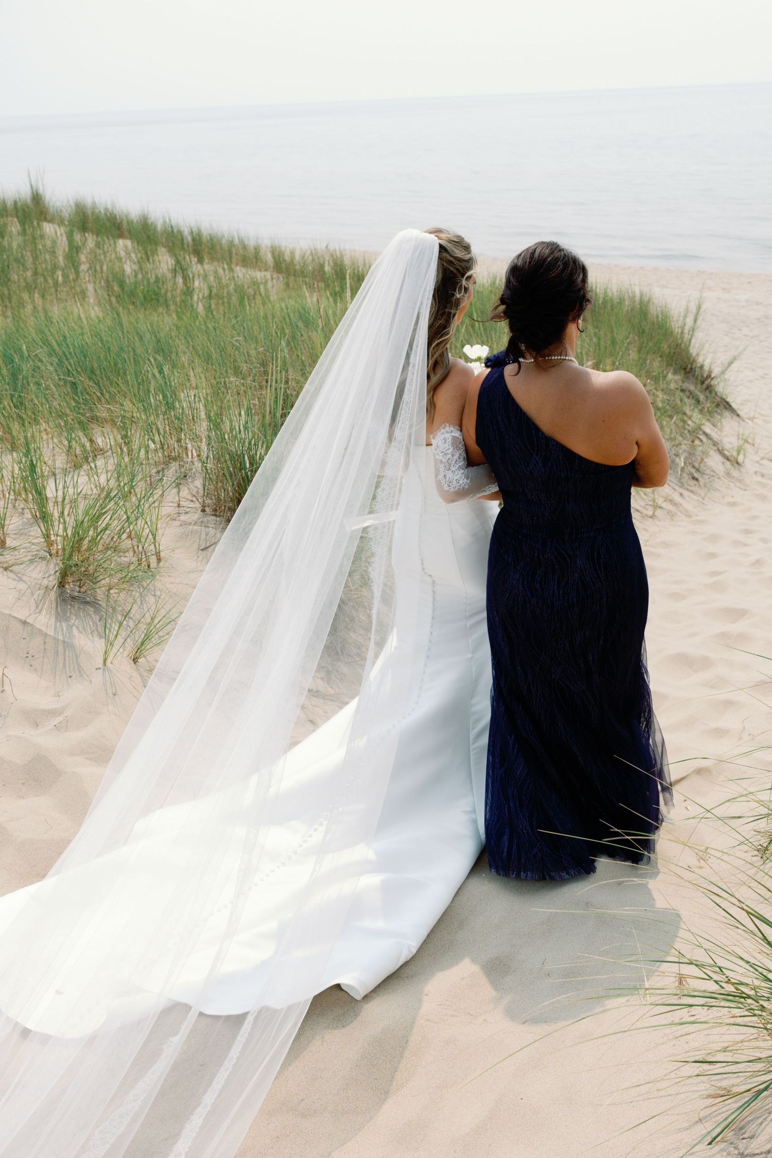 Long flowing white wedding veil trails in beach grass during coastal photoshoot.