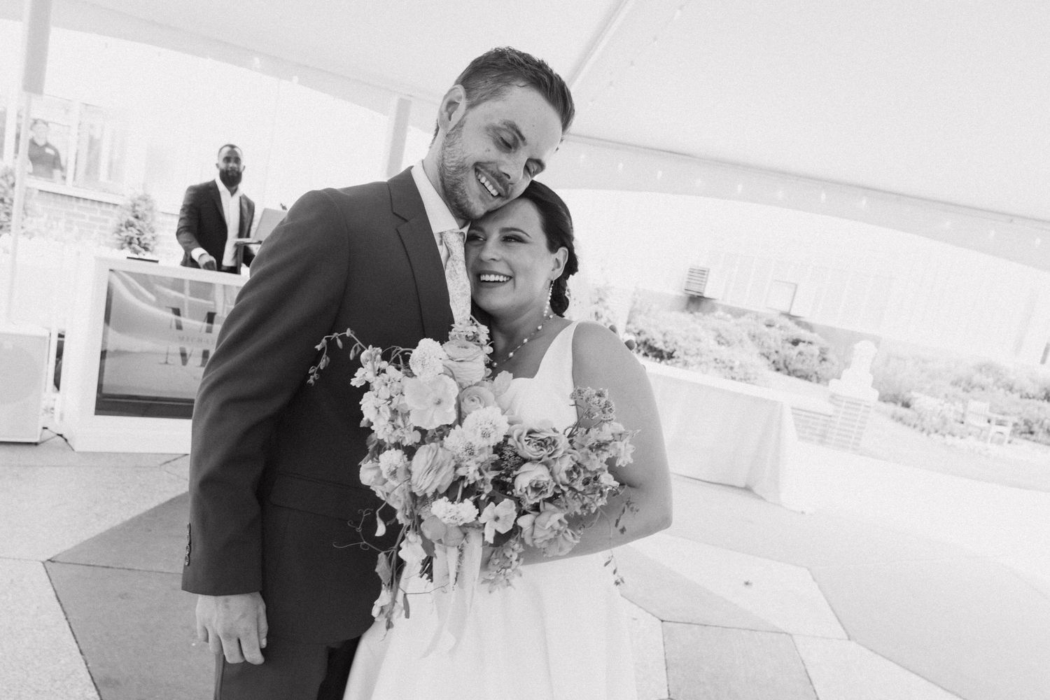 A romantic moment captured during a wedding ceremony under a white tent with floral decorations.