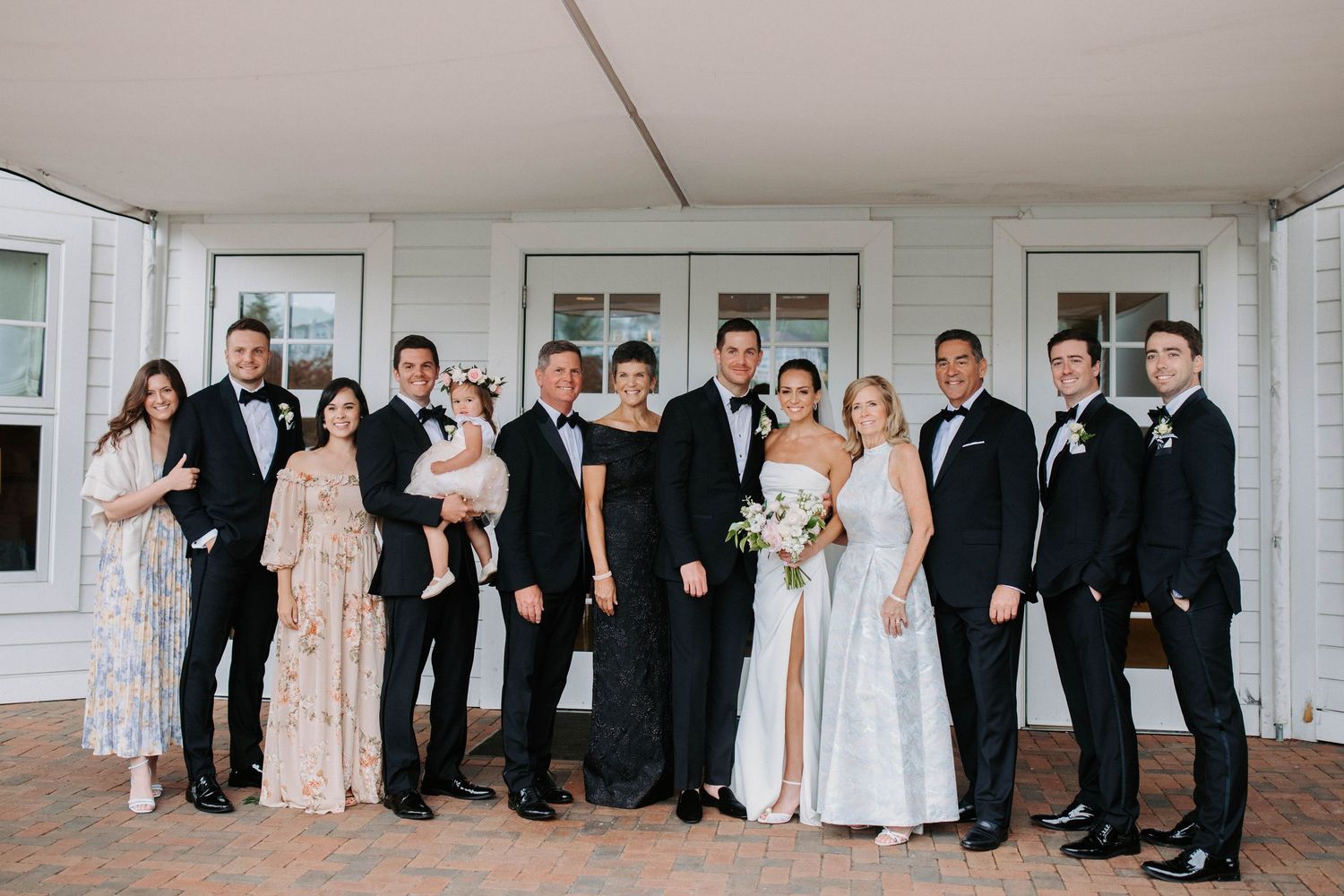Wedding party in formal attire poses together on white porch.