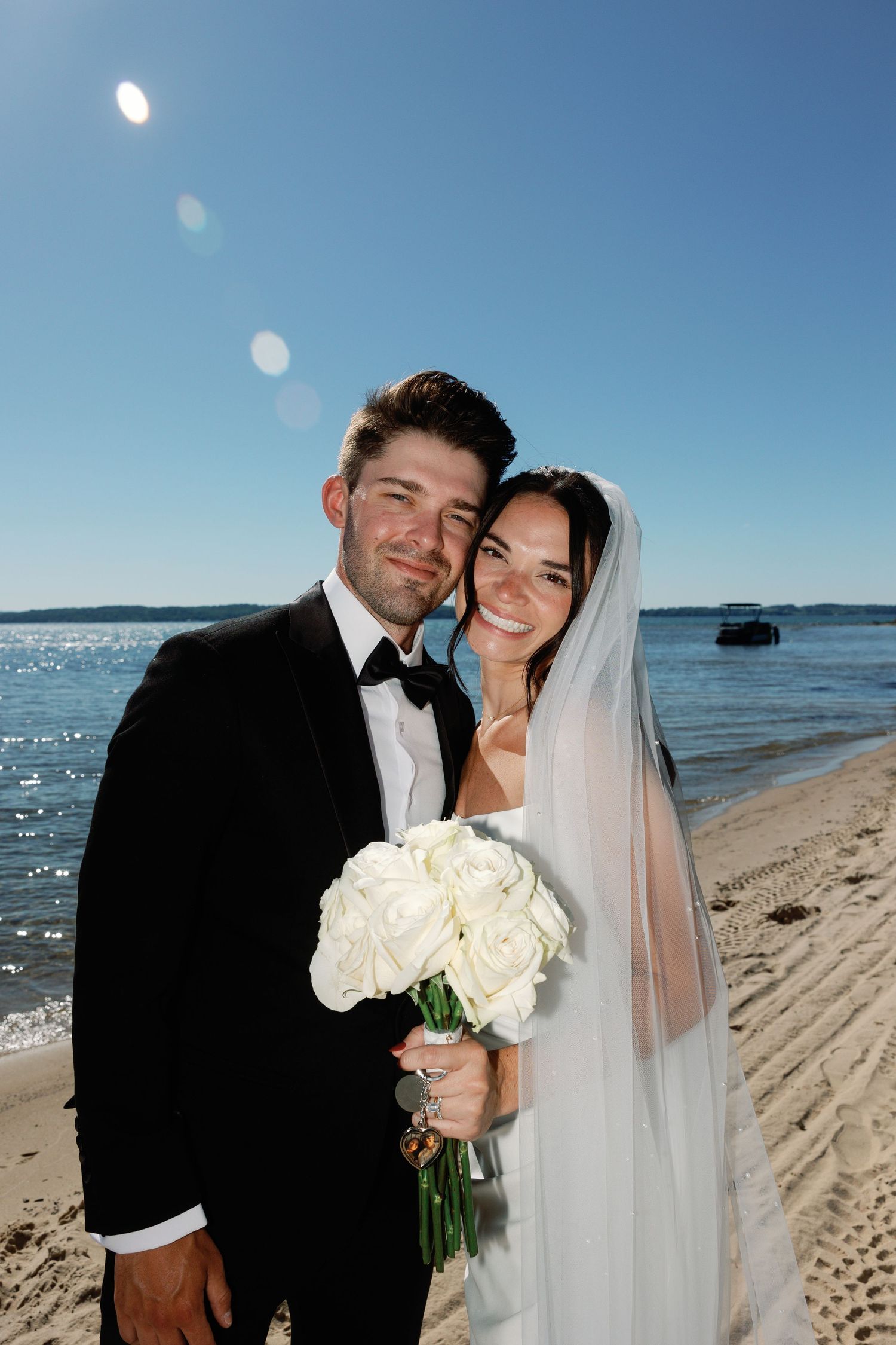 Bride and groom share romantic moments on a beach with sparkling water and blue skies in the background.
