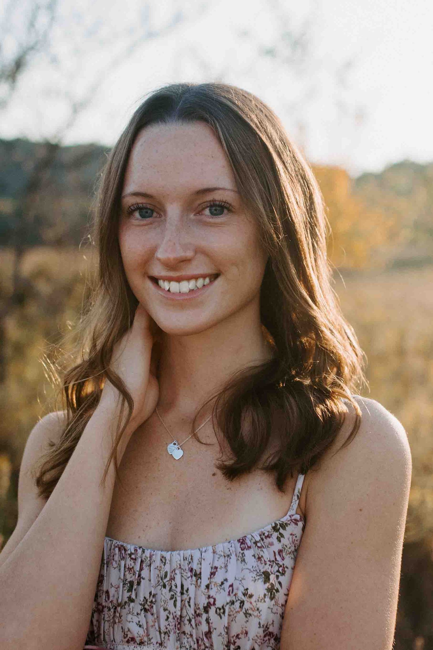 Portrait in a sunlit meadow wearing a floral dress with warm evening light.