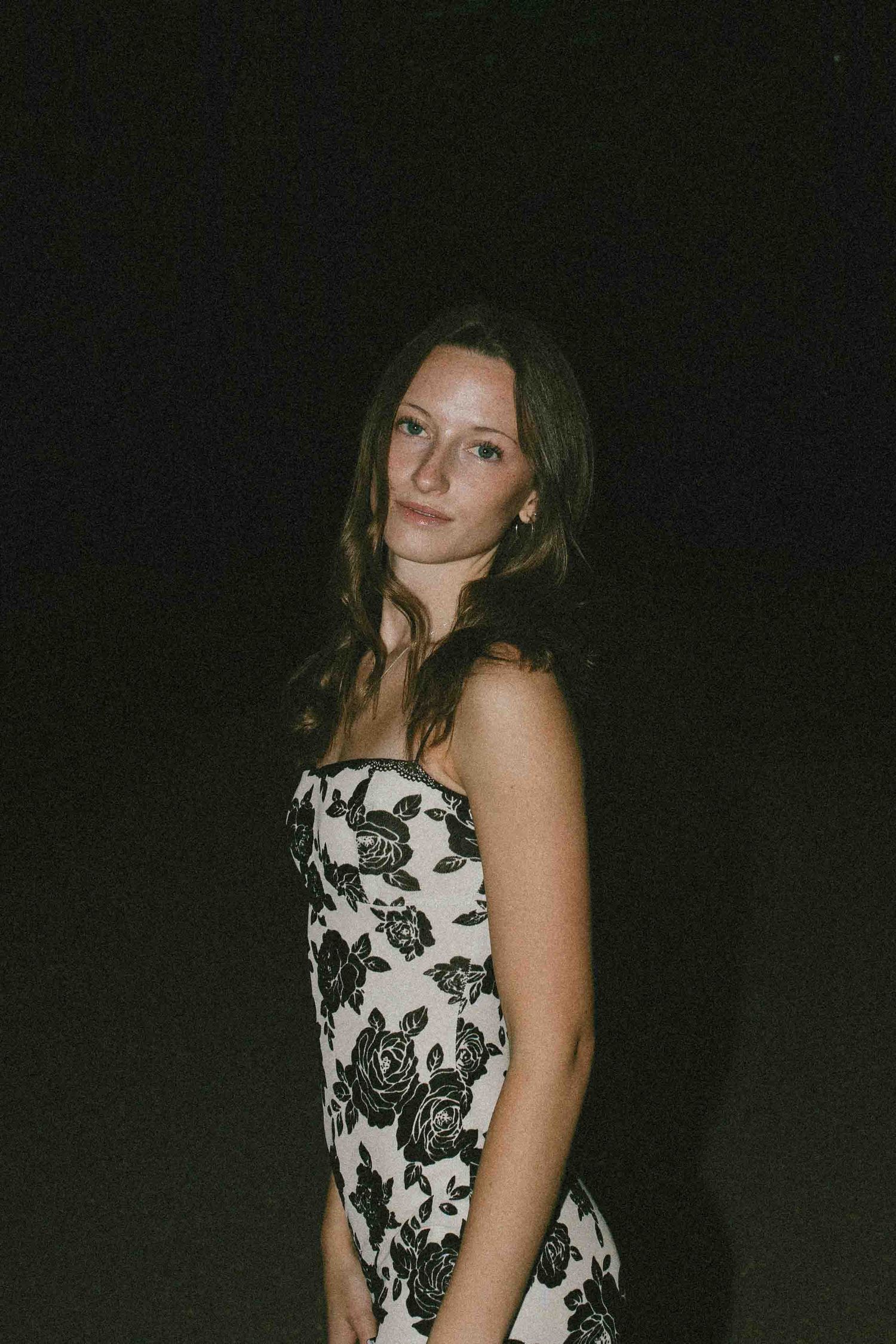 Dramatic nighttime portrait showcasing a black and white floral dress against a dark background.