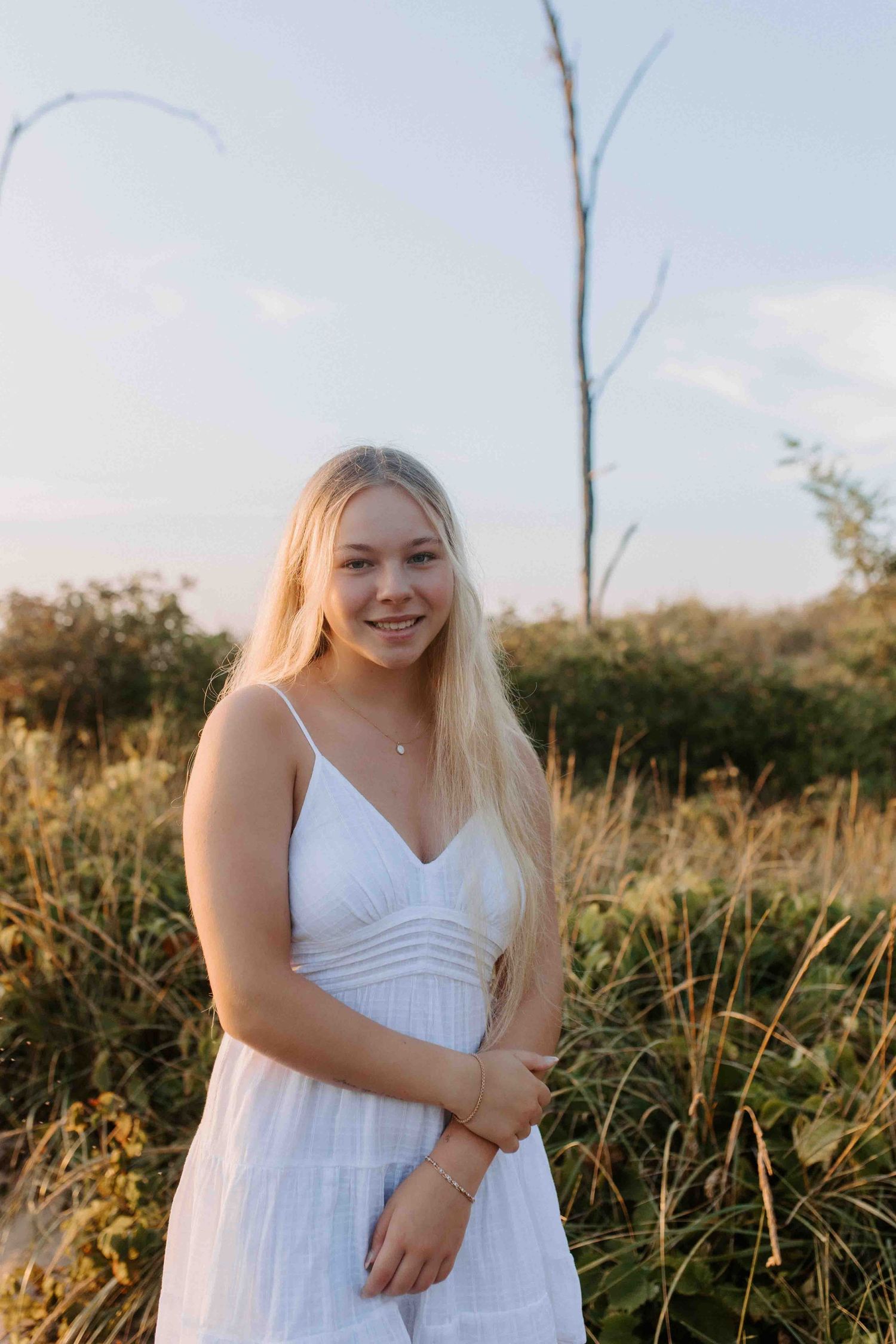 Person in white dress poses in golden hour lighting against natural backdrop.