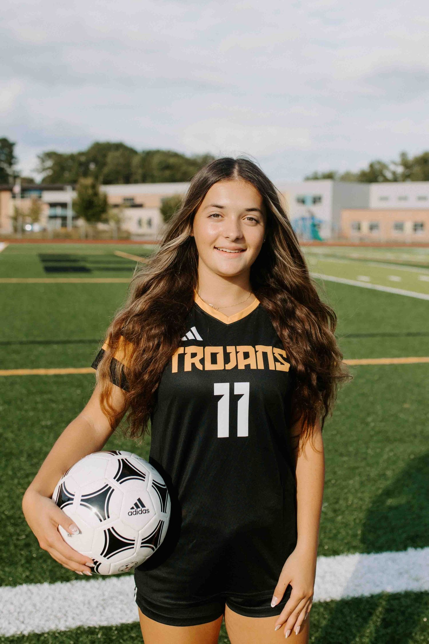 Soccer player poses with ball on field in black Trojans uniform number 11.