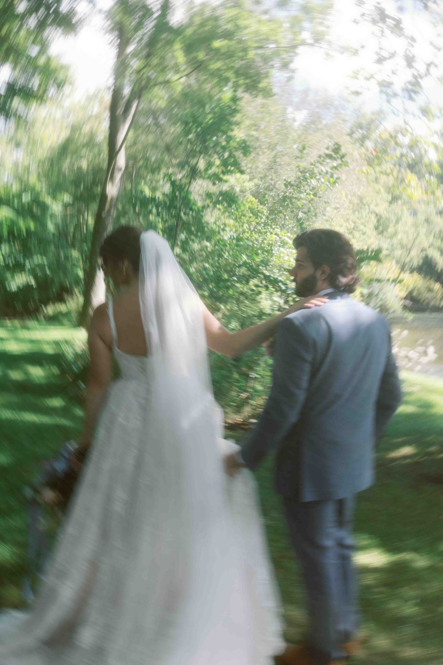 Dreamy motion-blur photo of a couple in wedding attire walking through a garden.